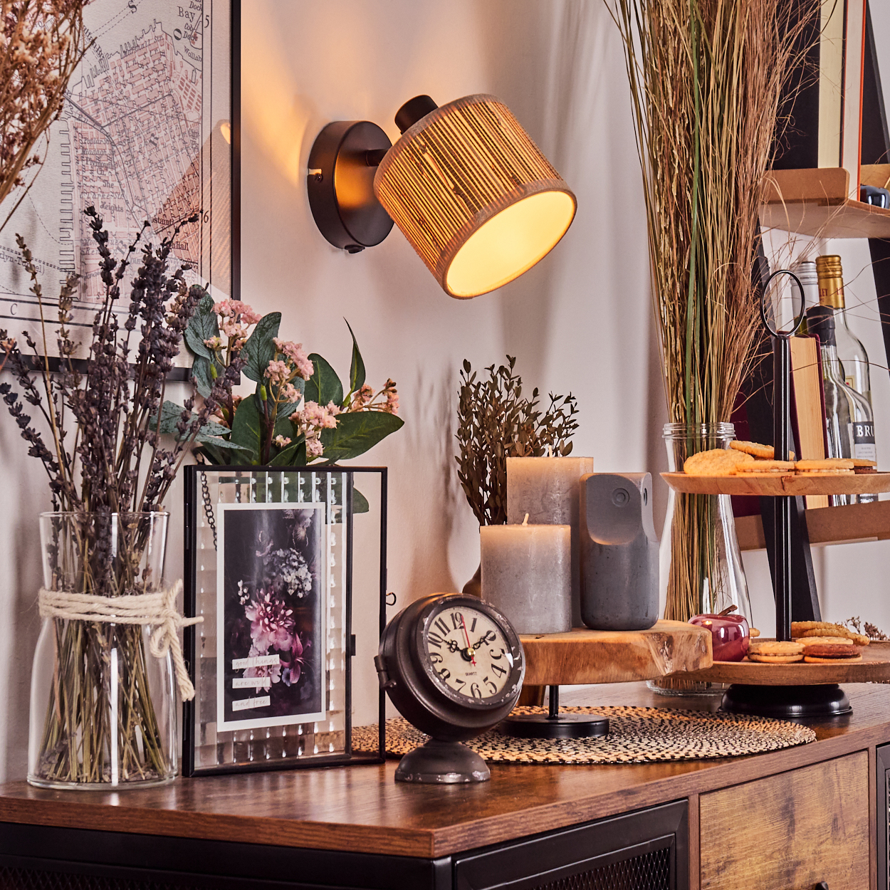 Zimmerszene mit Lampe, Uhr, Blumen, Kerzen, gerahmtem Bild und Dekorationsartikeln auf einem Holzschrank.