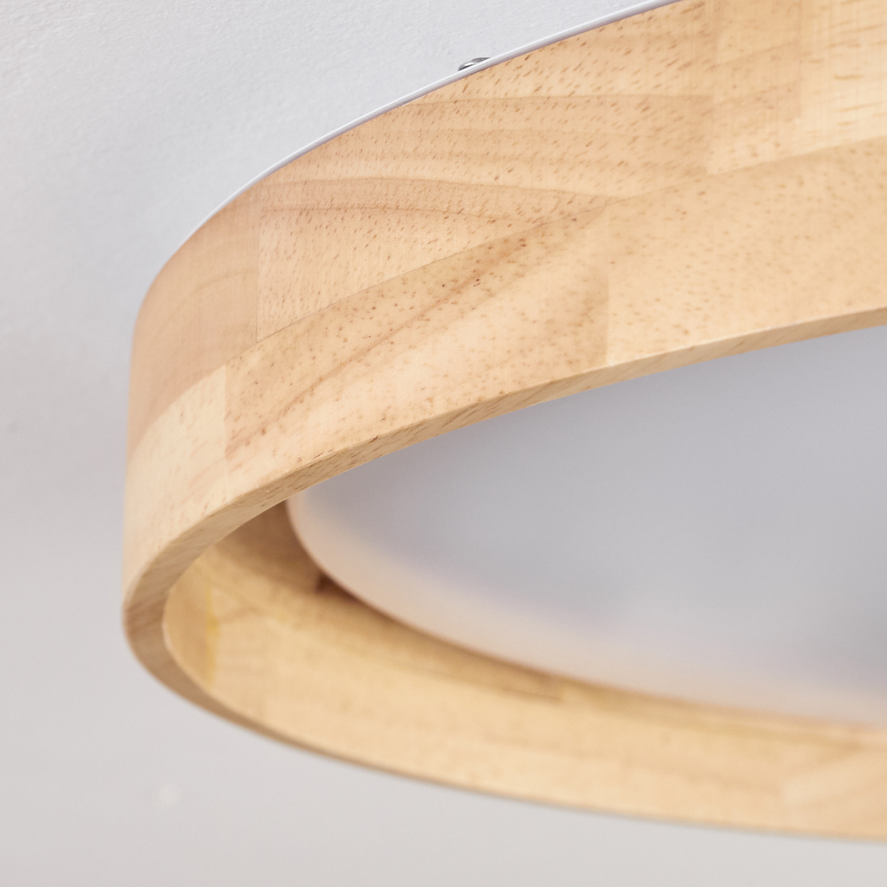 Nahaufnahme einer modernen Holzlampe. Die Lampe hat einen Holzrahmen und einen weißen Lichtdiffusor. Der Hintergrund ist eine weiße Wand.