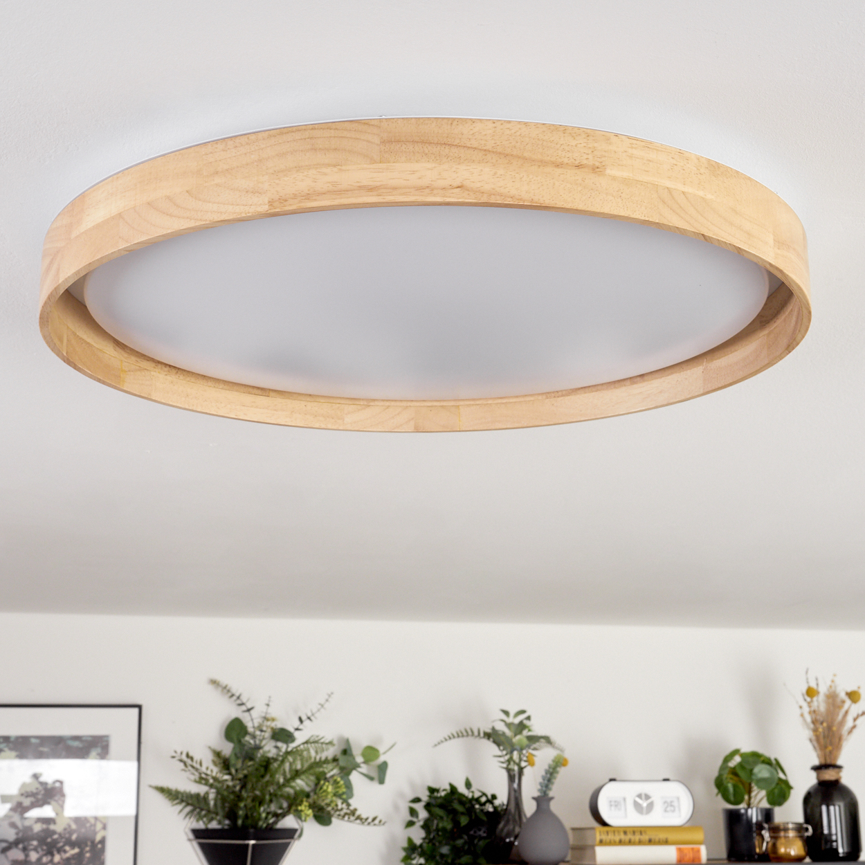 Eine runde Deckenleuchte aus Holz mit weißem Diffusor. Darunter befinden sich Pflanzen und Dekoration auf einem Regal.