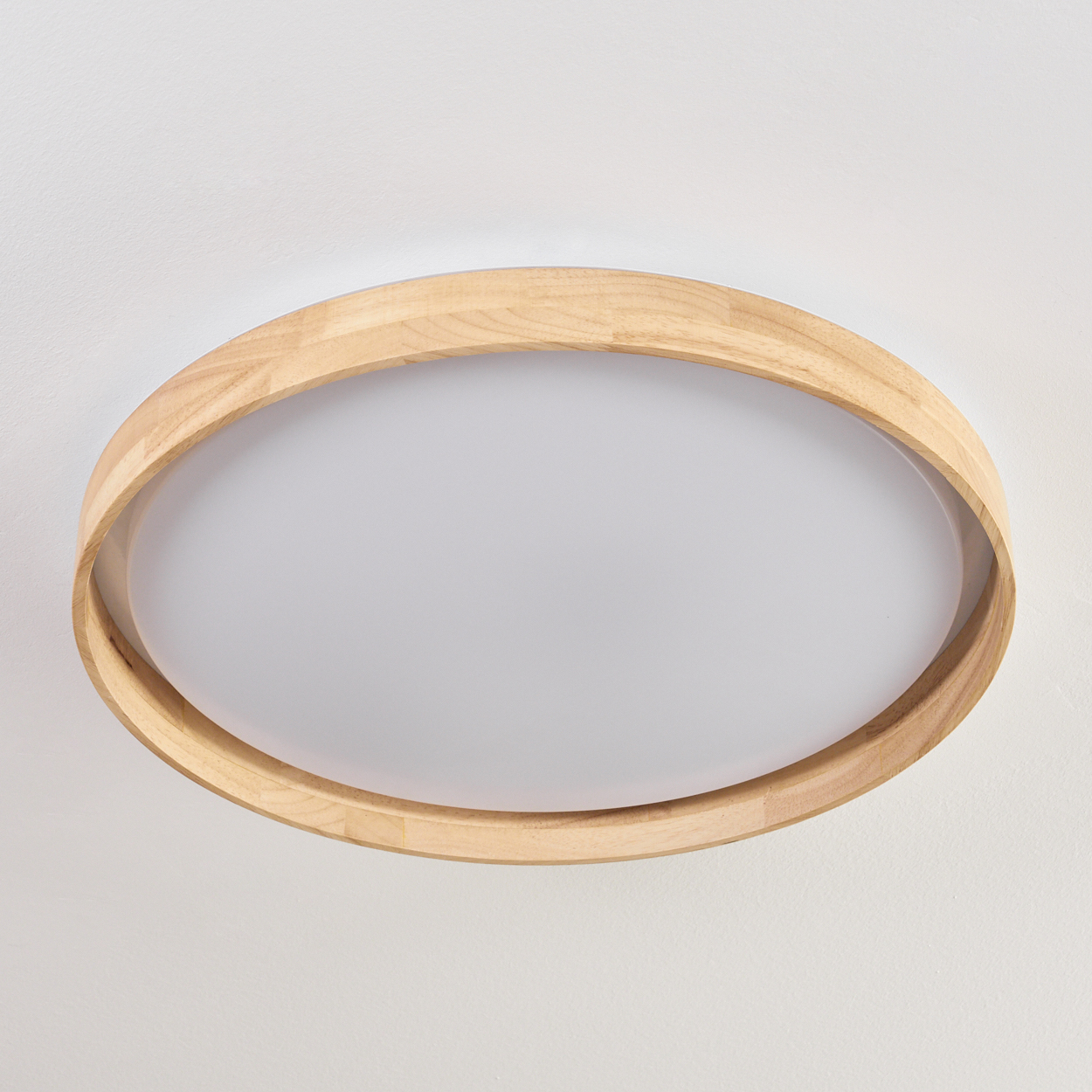 Eine runde Deckenleuchte. Sie hat einen hellen Holzrahmen und eine weiße, ovale Lichtabdeckung an einer weißen Decke.