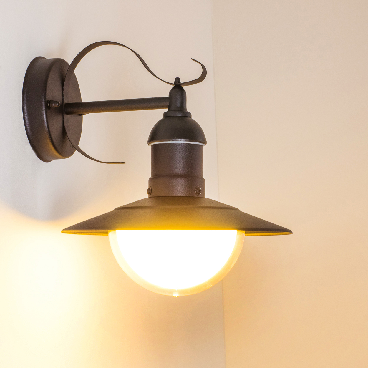 Eine an der Wand montierte Außenlampe. Sie ist schwarz und braun, mit einem nach unten gerichteten Schirm und einem hellen, warmfarbigen Licht.