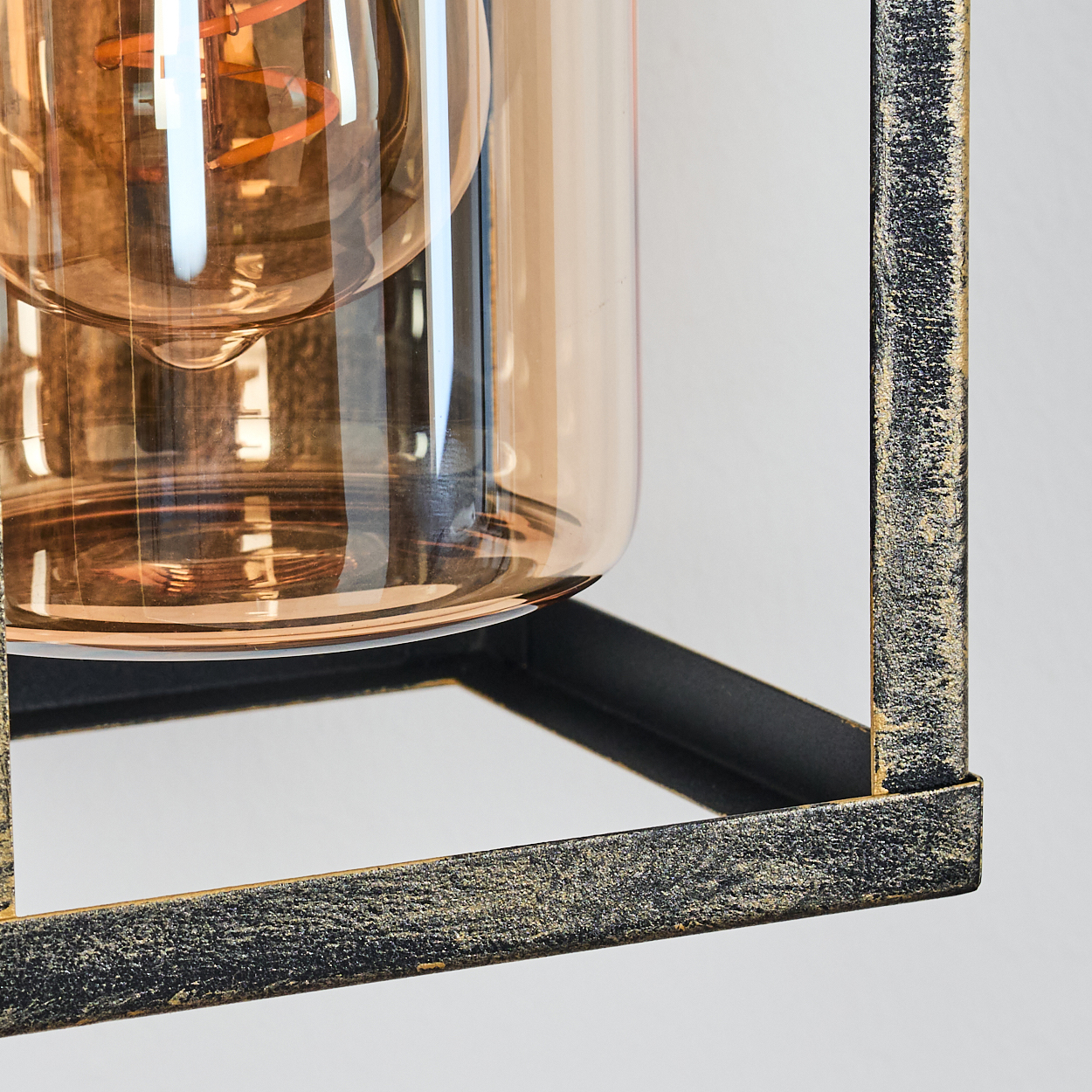 Nahaufnahme einer dekorativen Leuchte. Sie verfügt über ein braunes Glasgehäuse in einem schwarz-goldenen Metallrahmen vor weißem Hintergrund.