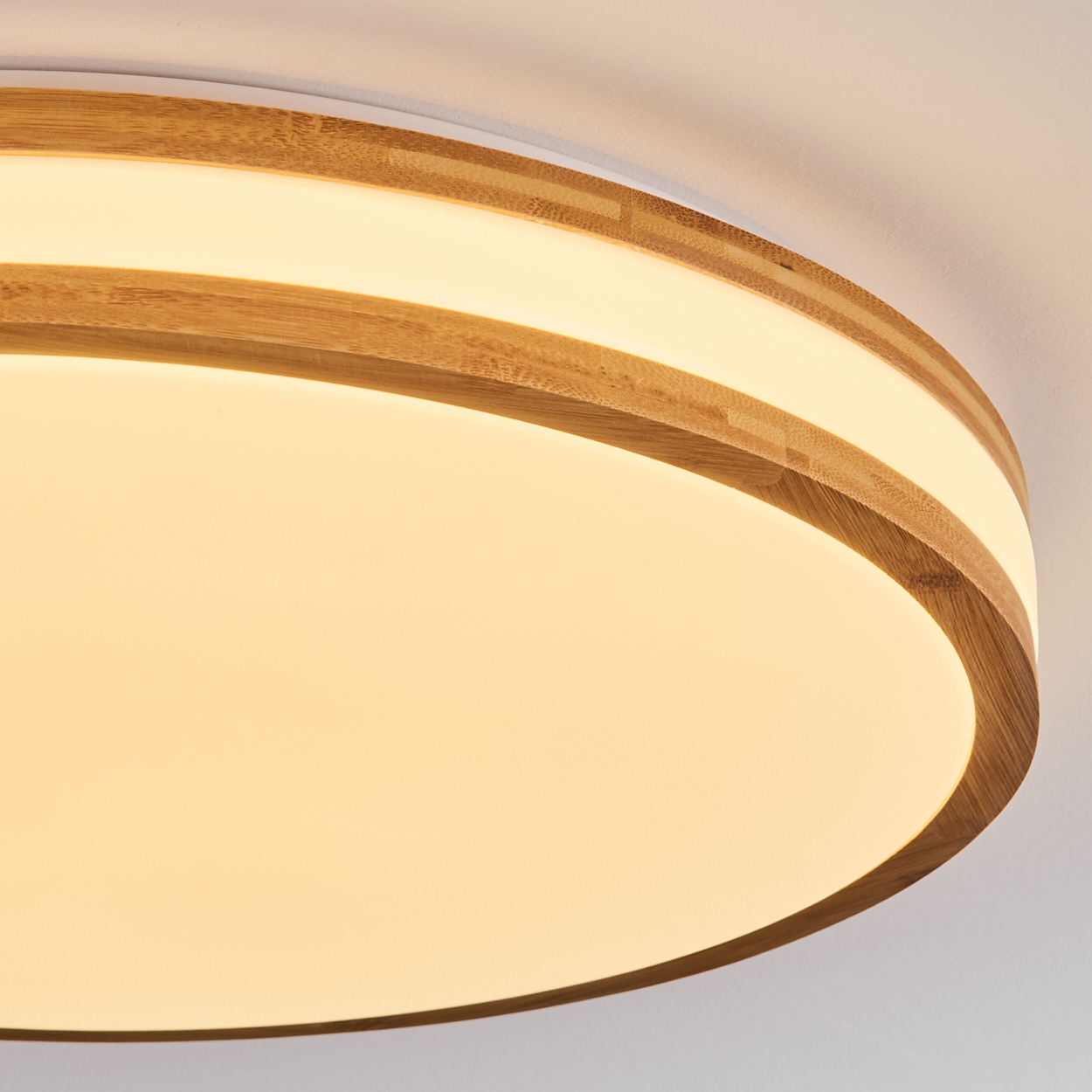 Eine runde Deckenlampe mit Holzrahmen und hellem, warmem Licht. Der Hintergrund ist eine schlichte weiße Decke.