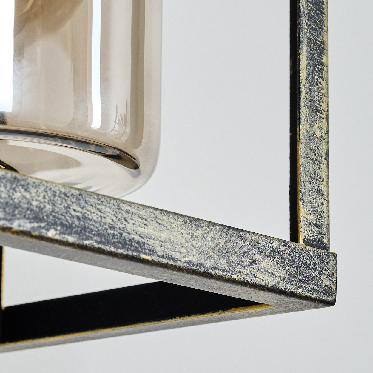 Nahaufnahme einer dekorativen Leuchte. Sie hat einen gold-schwarzen Metallrahmen mit einem Glaskylinder darin.