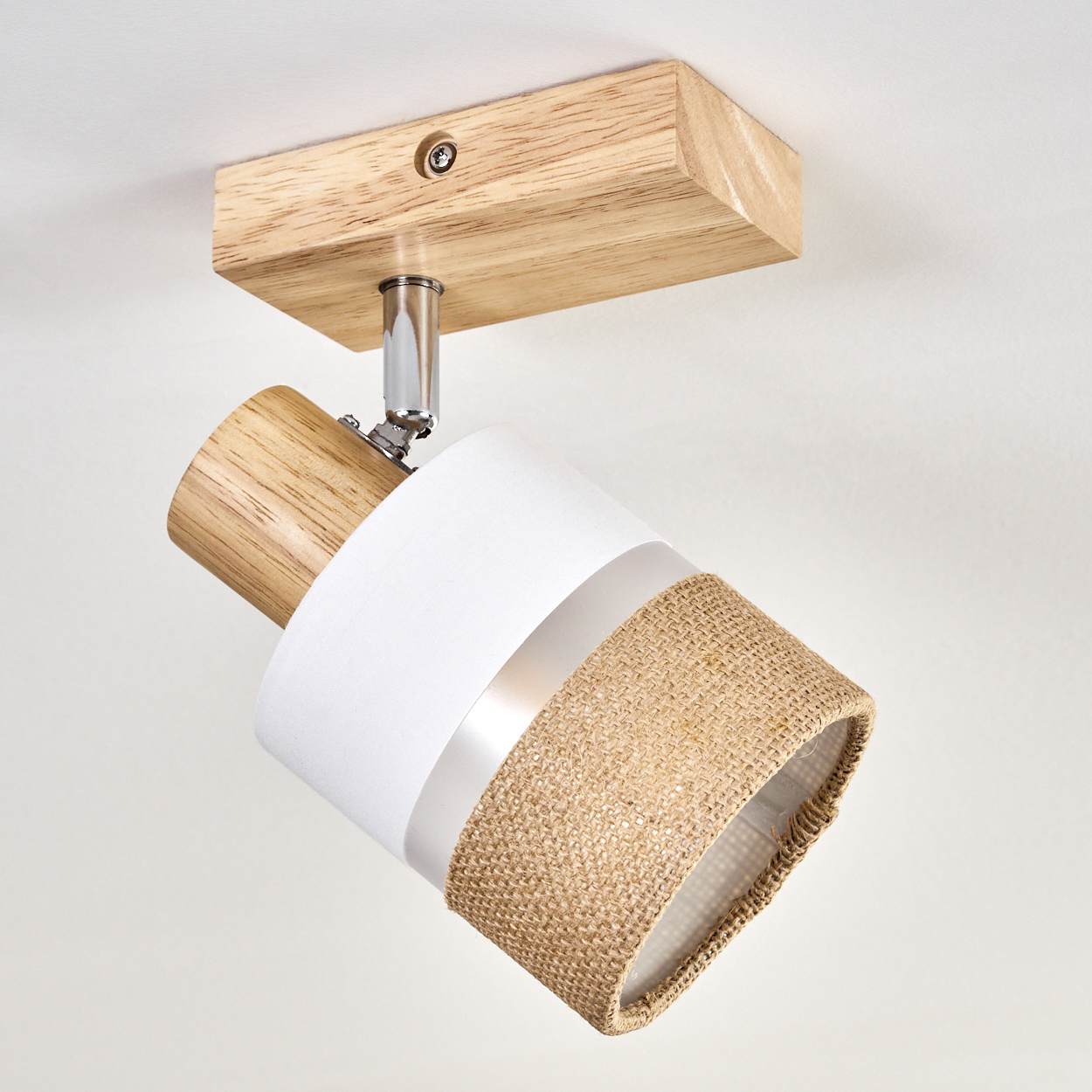 Deckenstrahler mit Holzsockel und zylindrischer Lampe. Die Lampe ist weiß, mit einem Lampenschirm aus Jute und silbernem Ring.
