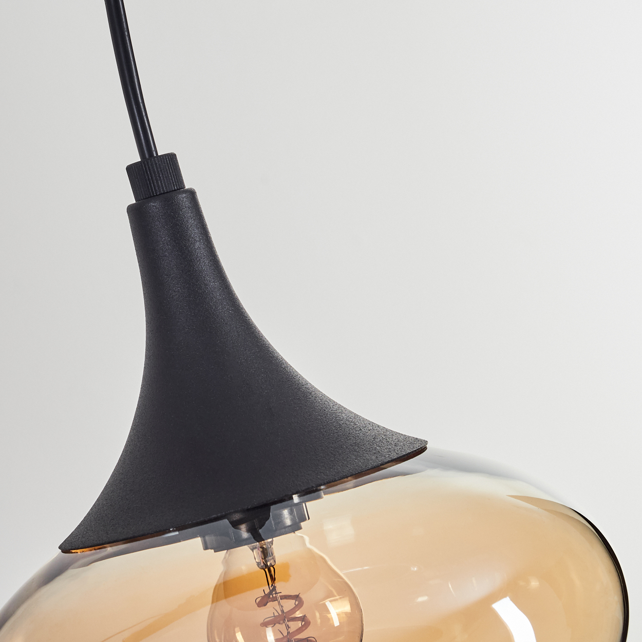 Eine schwarze Pendelleuchte mit Glasschirm. Die Glühbirne ist sichtbar. Der Hintergrund ist weiß.