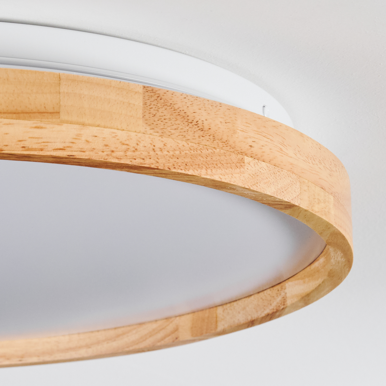 Nahaufnahme einer modernen Deckenlampe. Sie hat einen Holzrahmen um einen weißen Lichtdiffusor. Der Hintergrund ist eine weiße Wand.
