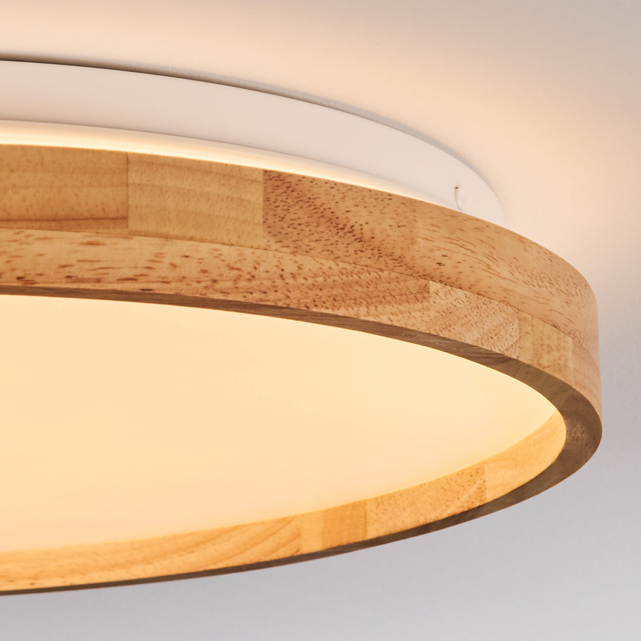 Nahaufnahme einer runden Deckenlampe aus Holz. Die Lampe hat einen weißen Rahmen und eine warme Lichtquelle. Das Holz hat eine natürliche, hellbraune Farbe.