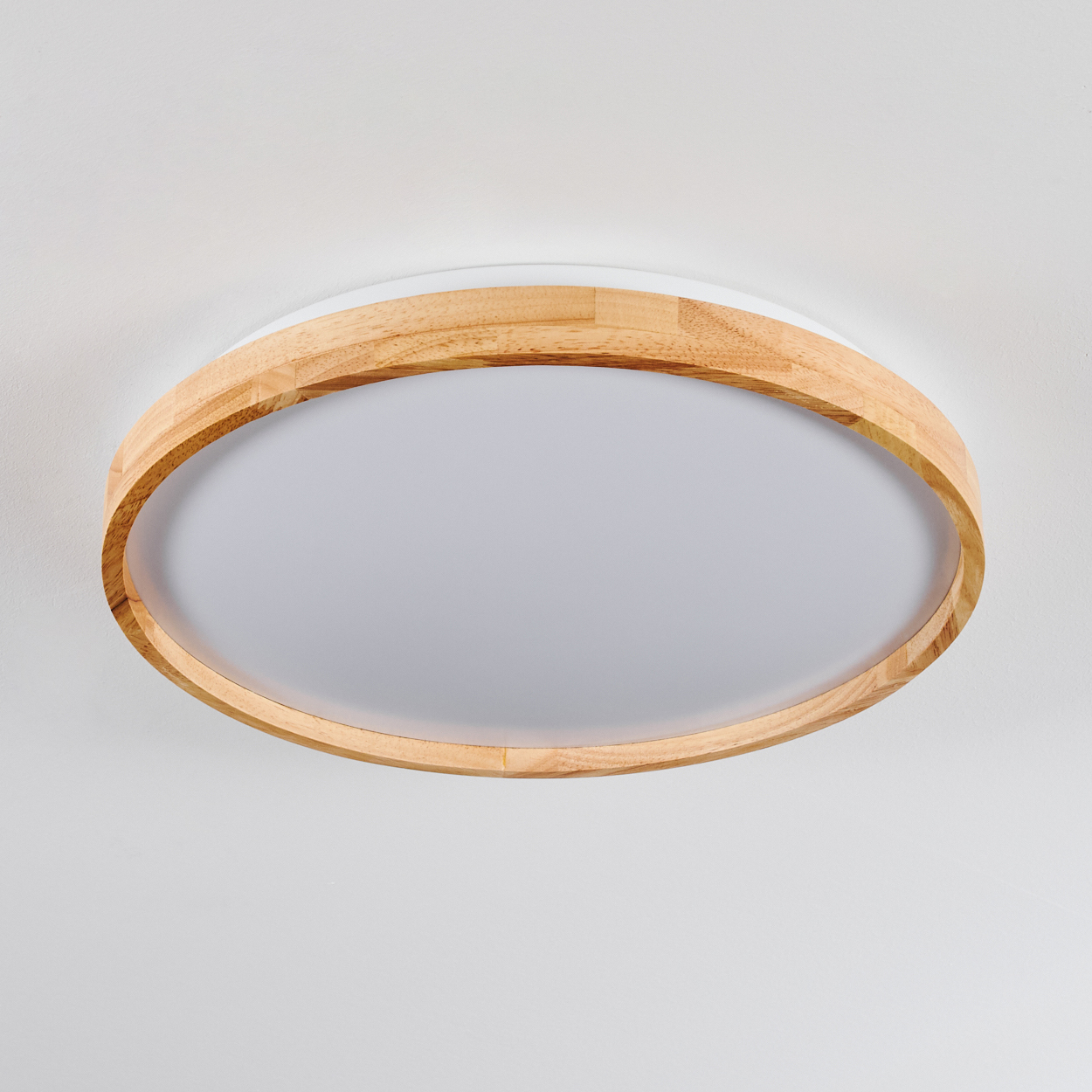 Eine runde Deckenleuchte mit Holzrahmen und weißem, mattiertem Glasdiffusor. Der Hintergrund ist eine weiße Decke.