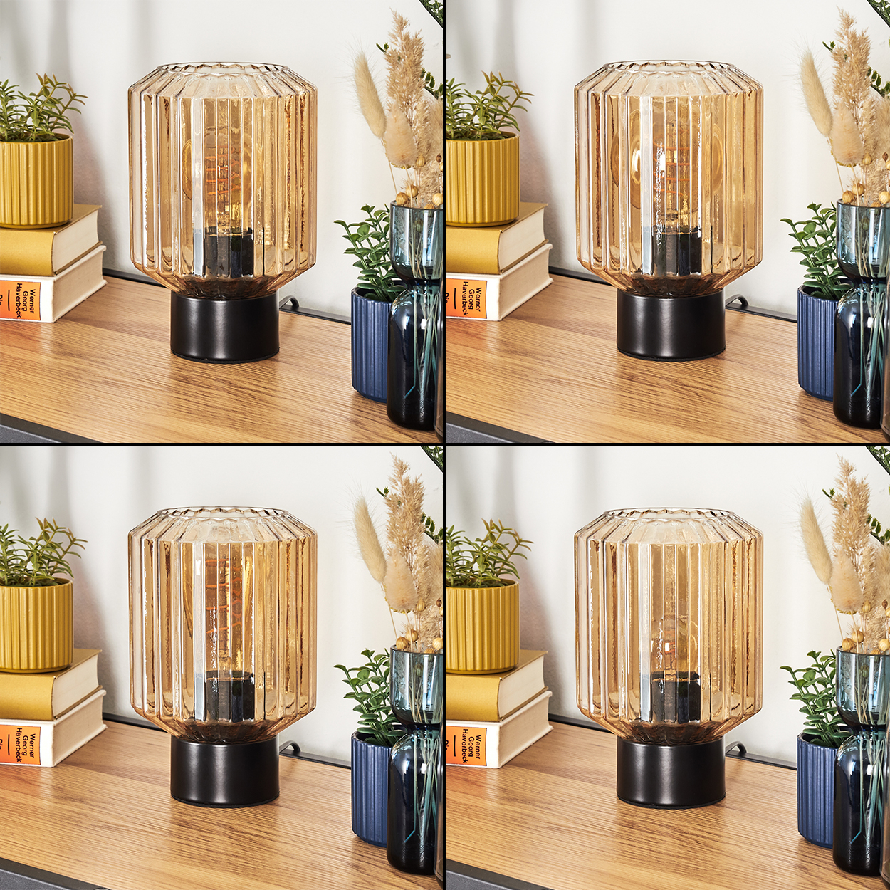 Eine Lampe mit Glasschirm und schwarzem Sockel steht auf einer Holzoberfläche. Pflanzen und Bücher sind im Hintergrund.