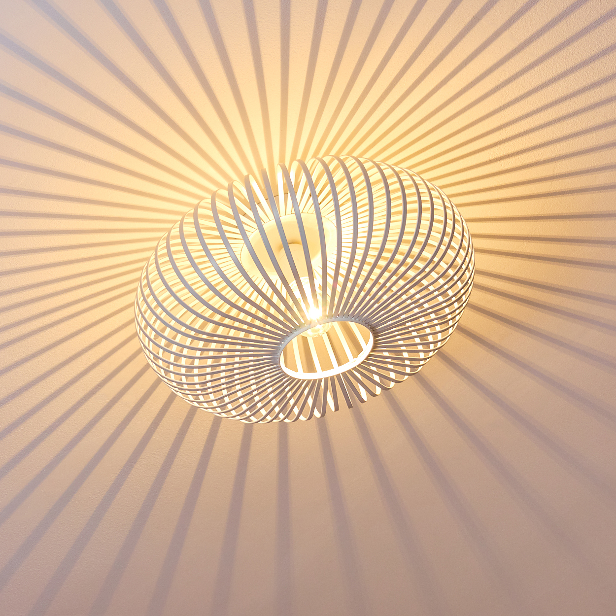 Eine weiße, kugelförmige Lampe hängt von der Decke und wirft radiale Schatten. Das Design der Lampe besteht aus gebogenen, parallelen Streben.