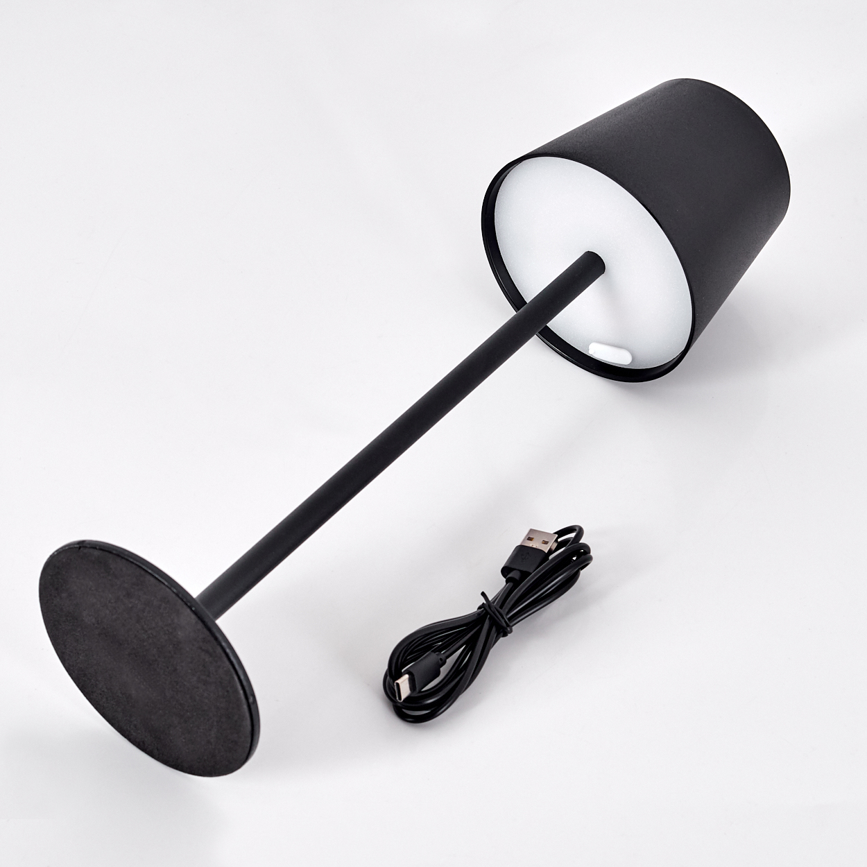Eine schwarze Schreibtischlampe mit zylindrischem Lampenschirm, schwarzem Ständer und USB-Kabel auf weißer Oberfläche.