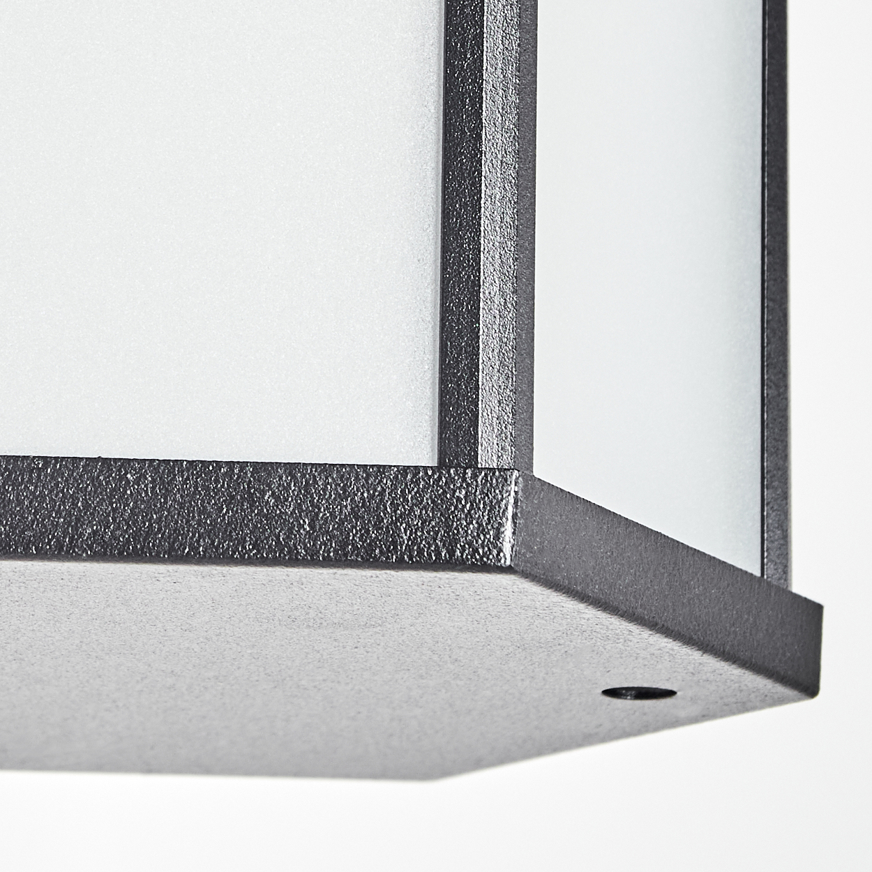 Nahaufnahme einer dunkelgrauen, strukturierten Metalllampe. Sie hat weiße Glasscheiben und befindet sich vor weißem Hintergrund.