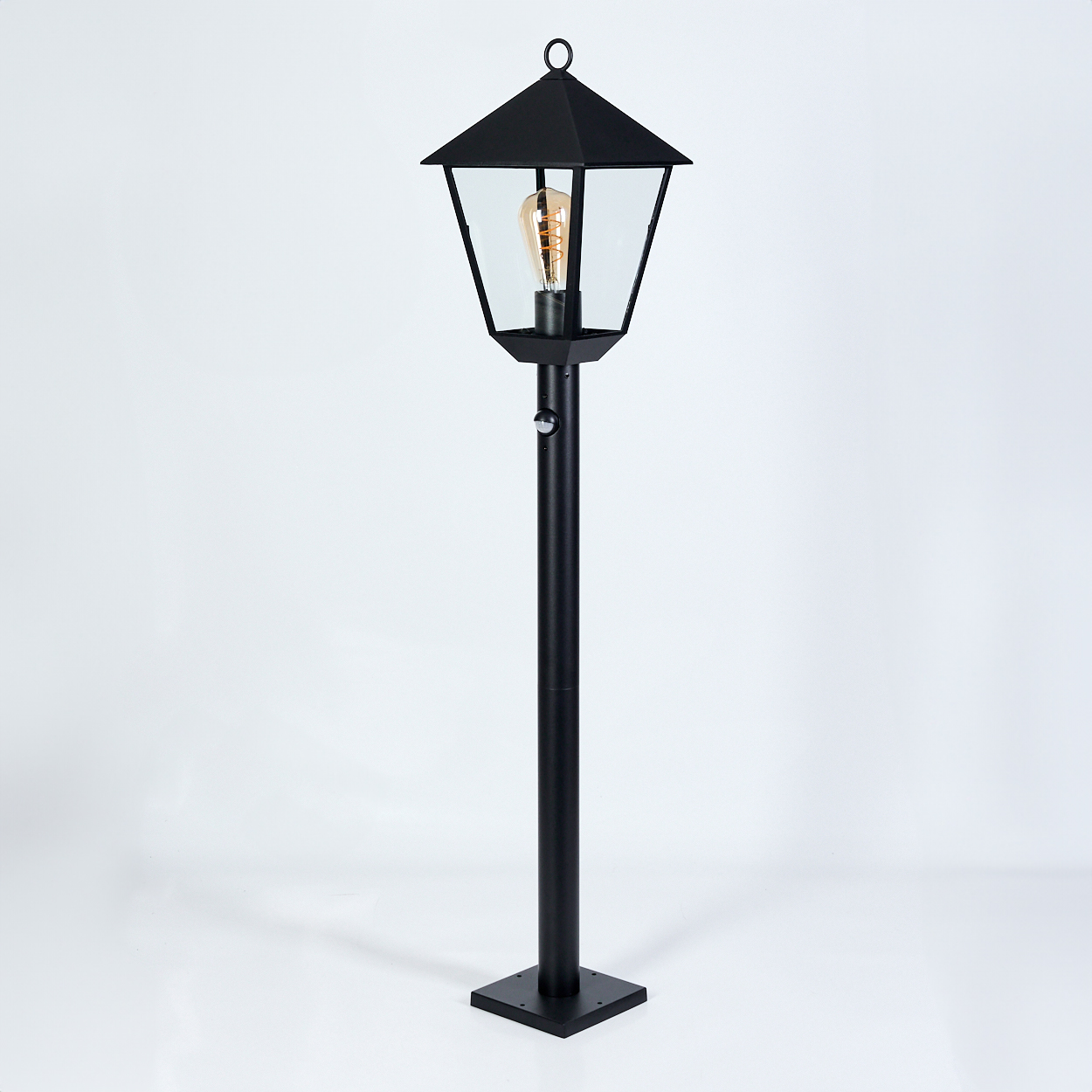 Eine schwarze Außenlaterne mit einem glaseingeschlossenen Licht und einer dekorativen Oberseite, vor weißem Hintergrund.