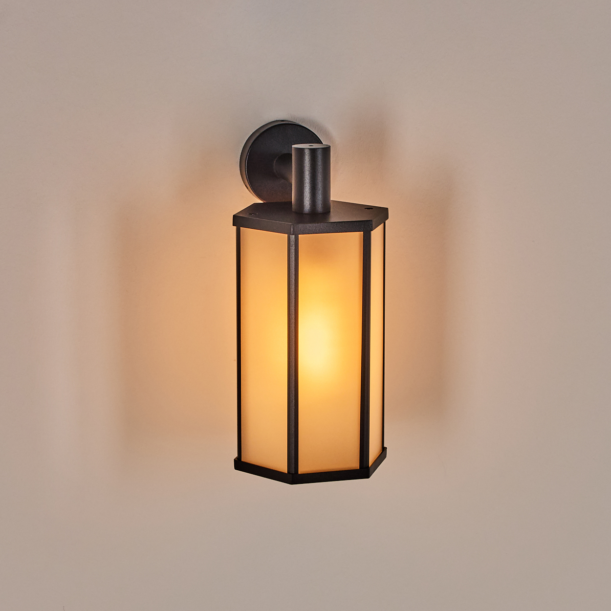 Schwarz-Wandlaterne mit Milchglasscheiben. Die Laterne ist beleuchtet und wirft ein warmes Licht auf die beige Wand.