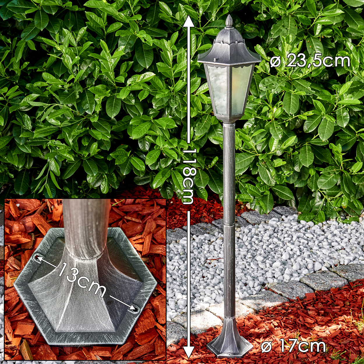 Eine graue Außenlampe mit grünem Blätterhintergrund. Die Lampe ist 118 cm hoch. Der Sockel steht auf roter Mulch, mit Steinbordüre.