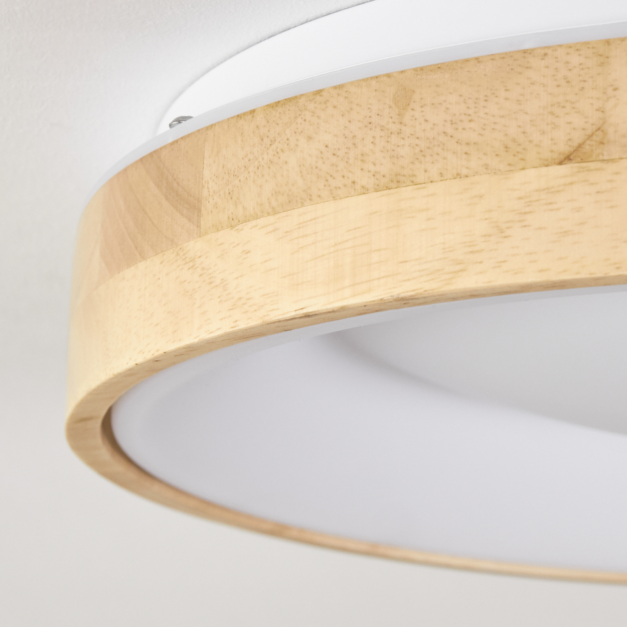 Nahaufnahme einer Deckenleuchte. Sie hat einen Holzring um einen weißen Lichtdiffusor, der an einer weißen Decke befestigt ist.