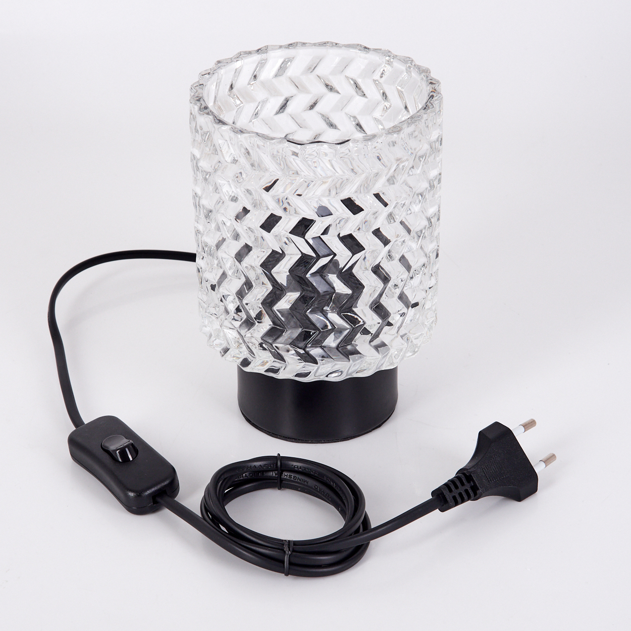 Eine Glaslampe mit gemustertem Schirm und schwarzem Sockel steht auf weißem Untergrund, mit schwarzem Kabel und Stecker.