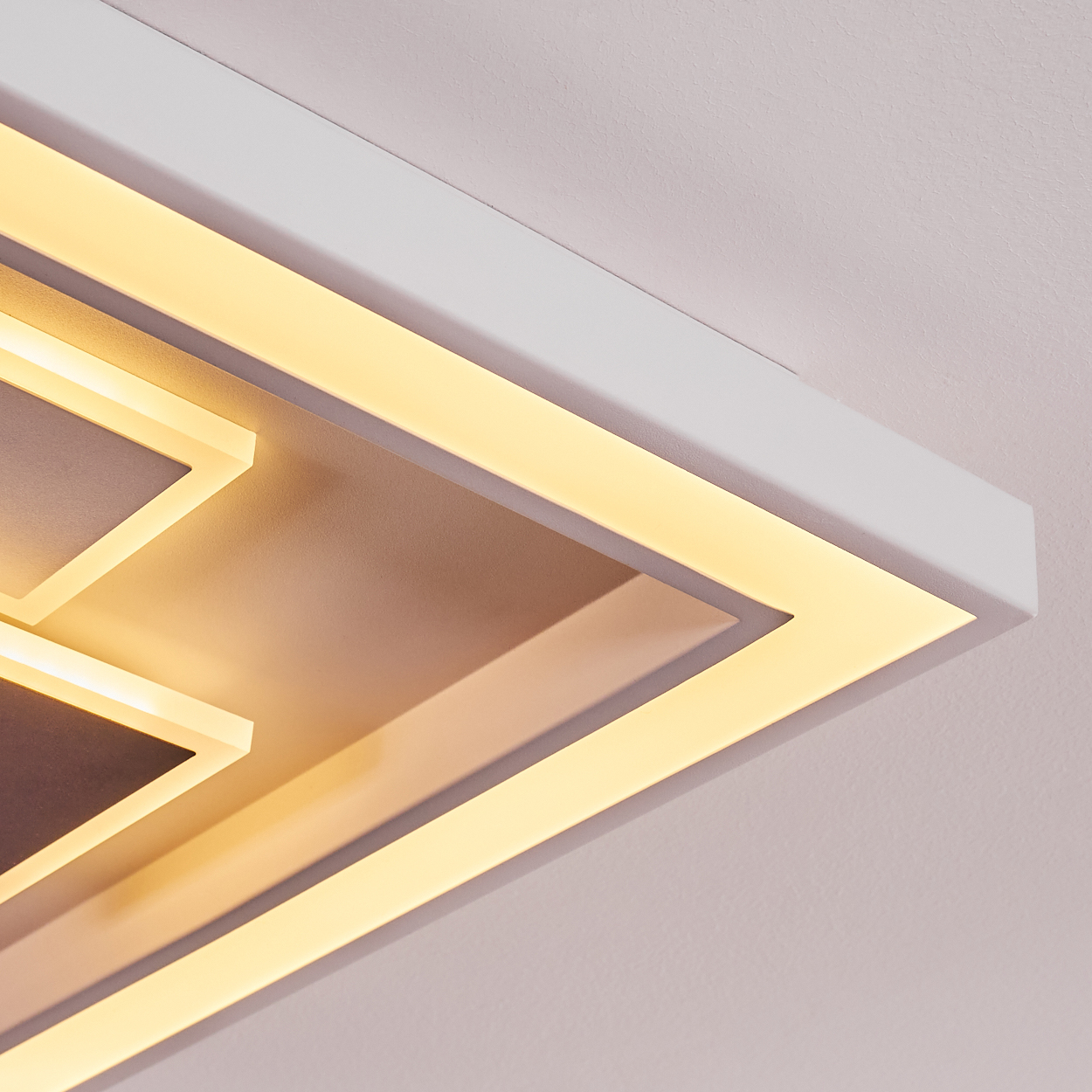 Nahaufnahme einer modernen Deckenleuchte. Sie hat einen weißen Rahmen mit warmgelben LED-Leuchten und ein geometrisches Design.