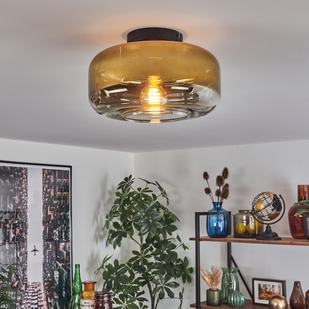 Eine Deckenlampe mit bernsteinfarbenem Glas. Pflanzen und Regale mit Dekor im Hintergrund. Helles Licht der Lampe erhellt den Raum.