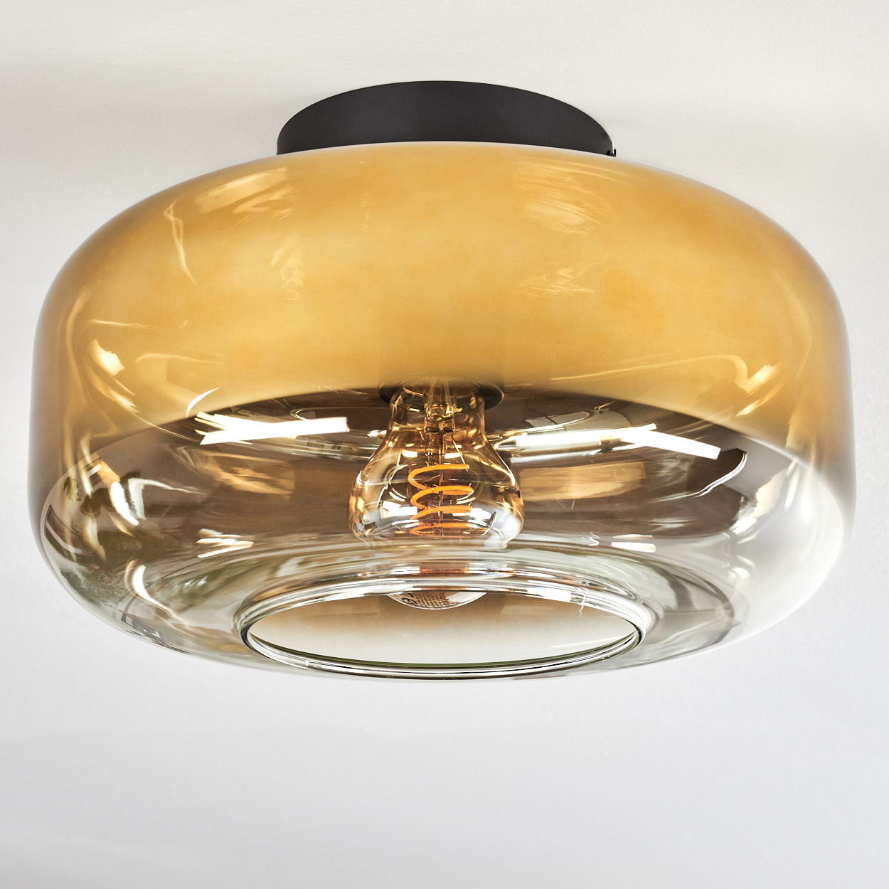 Eine moderne Deckenleuchte. Sie hat einen runden Glasschirm in bernsteinfarbener Farbe. Im Inneren befindet sich eine sichtbare Wendelglühbirne.