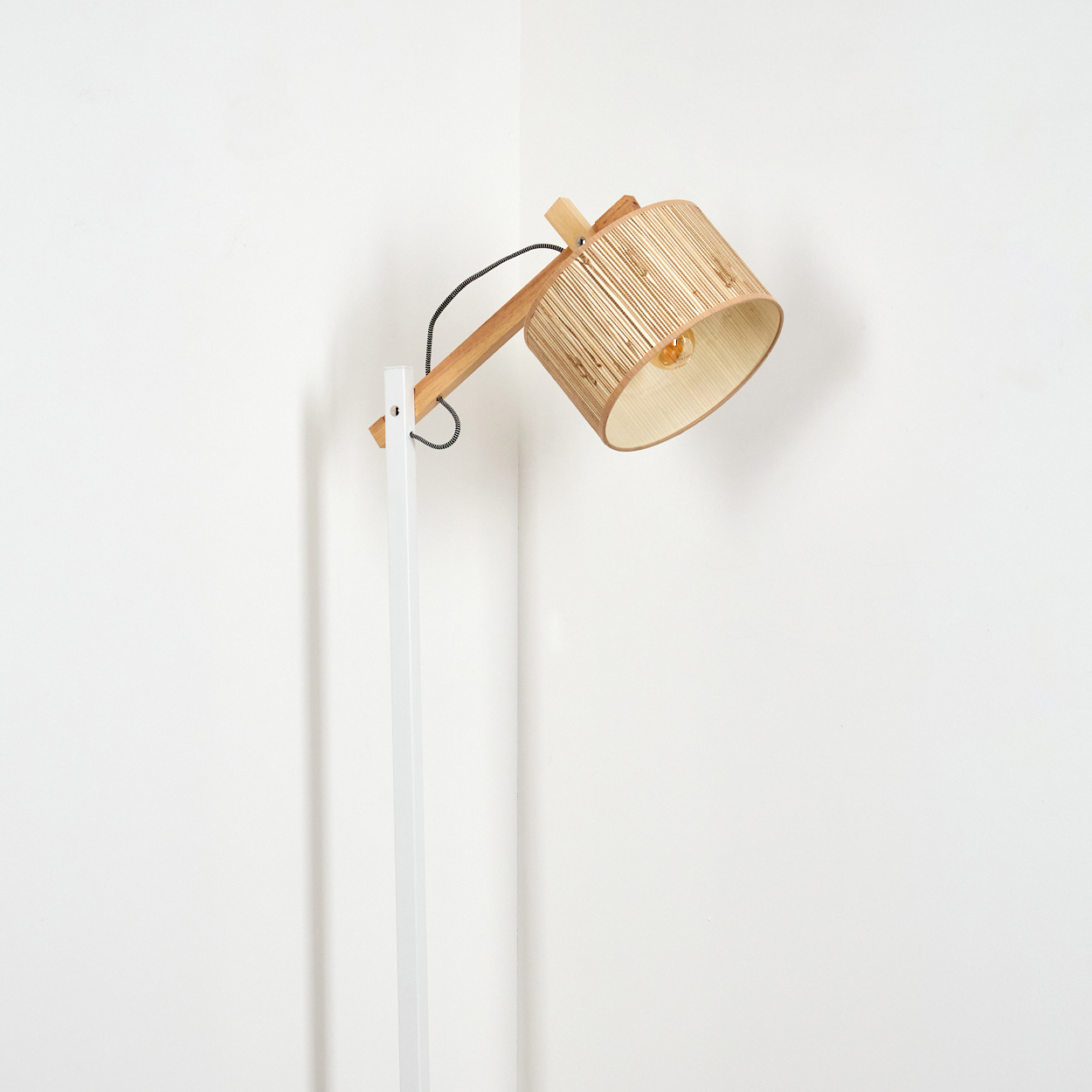 Eine Stehlampe mit Holzrahmen und Bambus-Lampenschirm steht in der Ecke eines weißen Raumes.