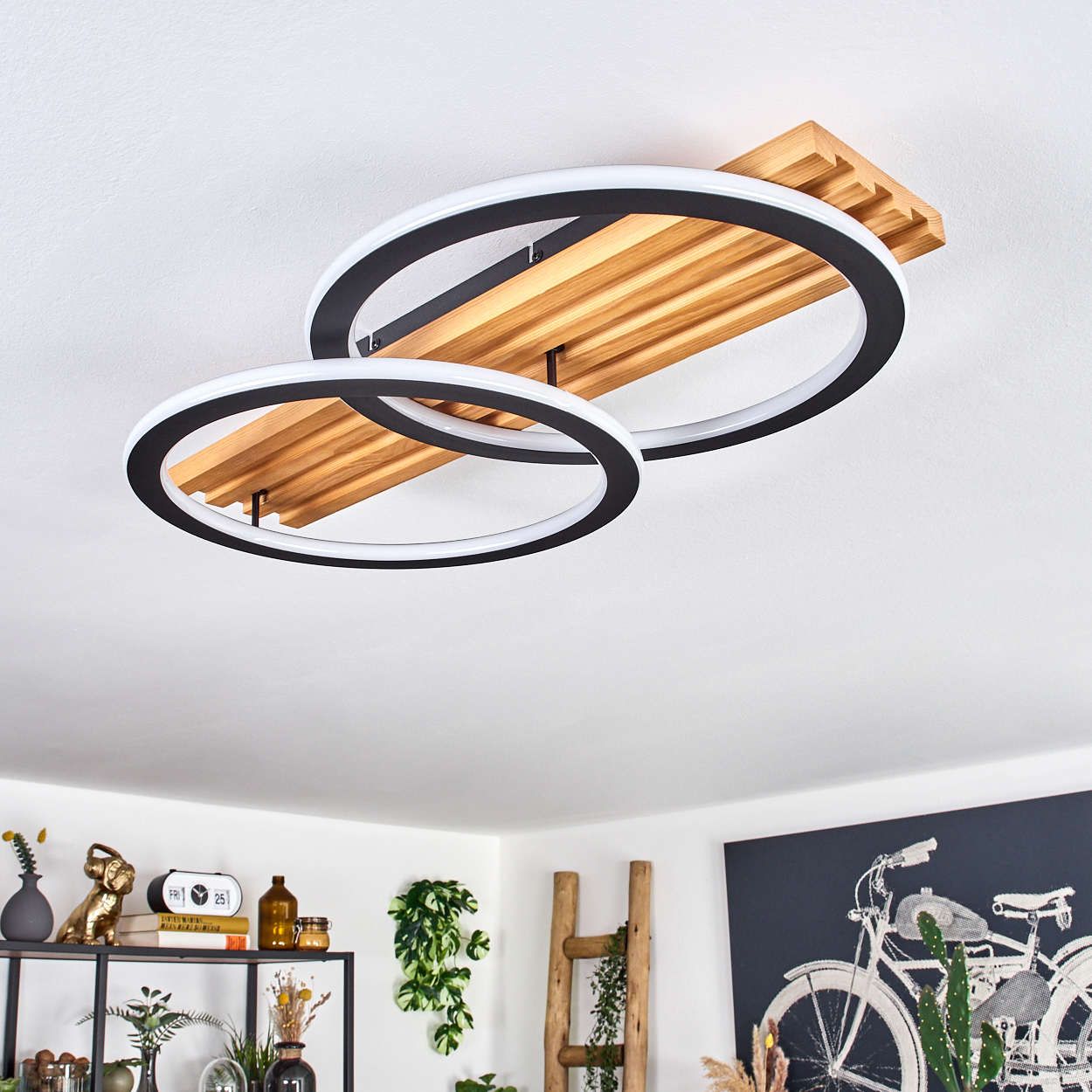 Moderne Deckenleuchte mit zwei schwarz umrandeten, weiß beleuchteten Ringen, Holzpaneel und sichtbaren Gegenständen auf dem Regal.