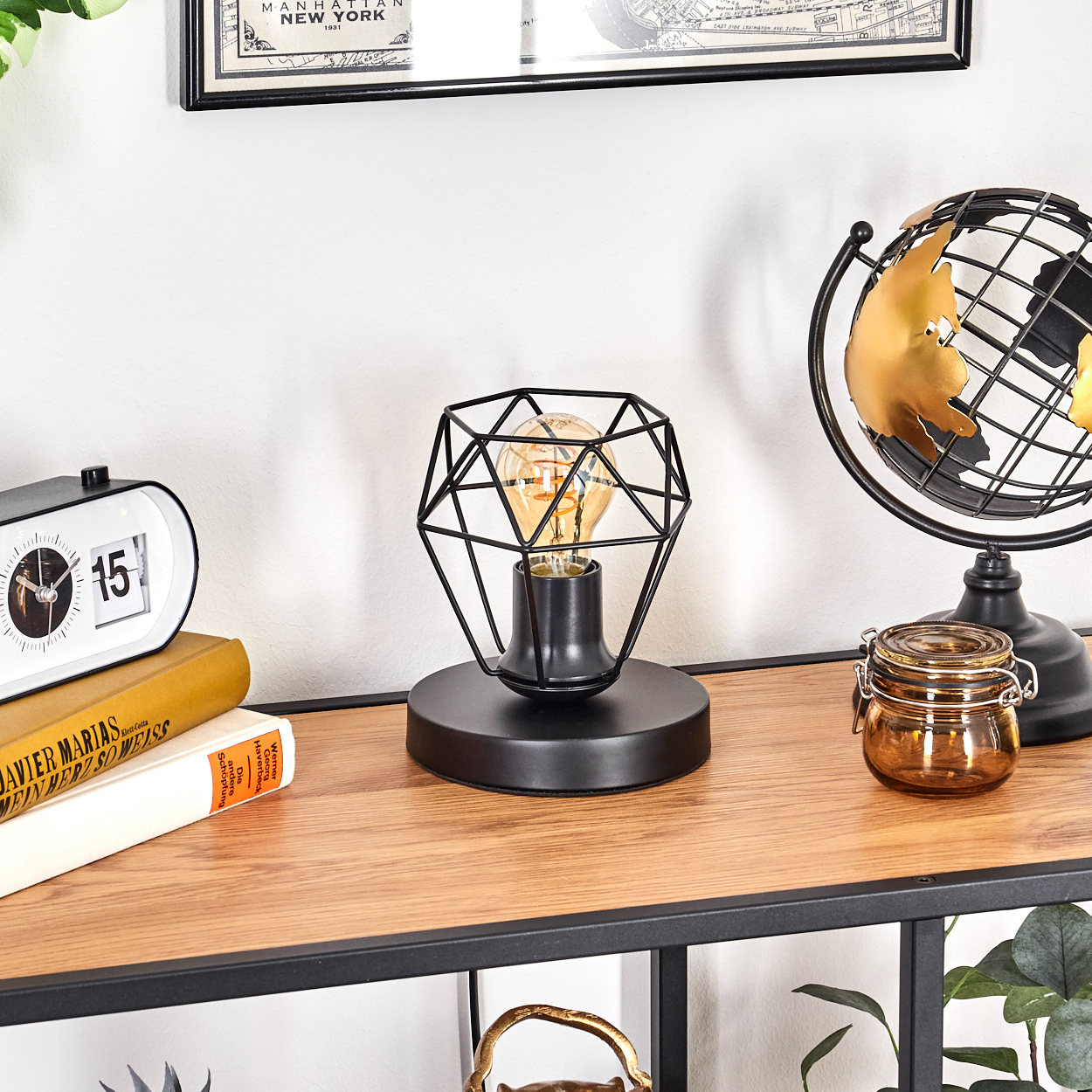 Ein Tisch mit schwarzer Lampe, Globus, Uhr, Büchern und Glas. Die Lampe hat einen geometrischen Käfig um eine Glühbirne.