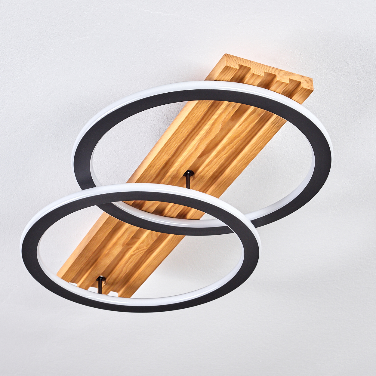 Eine Deckenleuchte mit zwei sich kreuzenden schwarzen und weißen Ringen. Sie ist auf einer Holzplatte an einer weißen Decke befestigt.