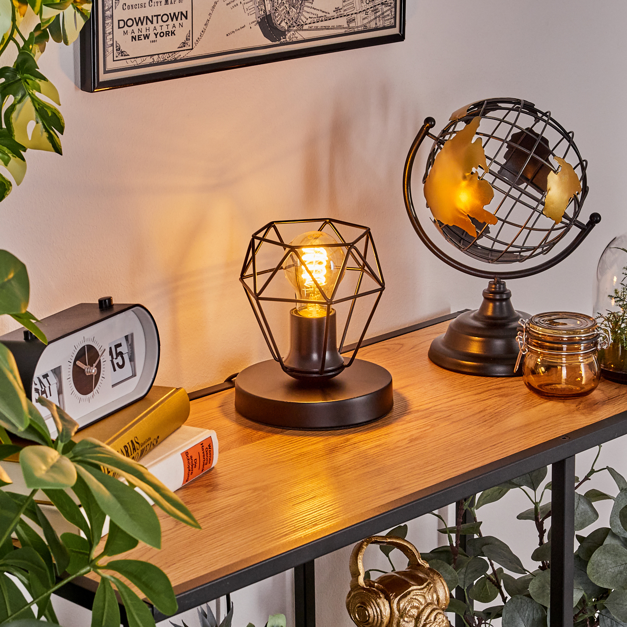 Ein Tisch mit Lampe, Globus und Uhr. Grüne Pflanzen im Vordergrund und eine Karte an der Wand im Hintergrund.