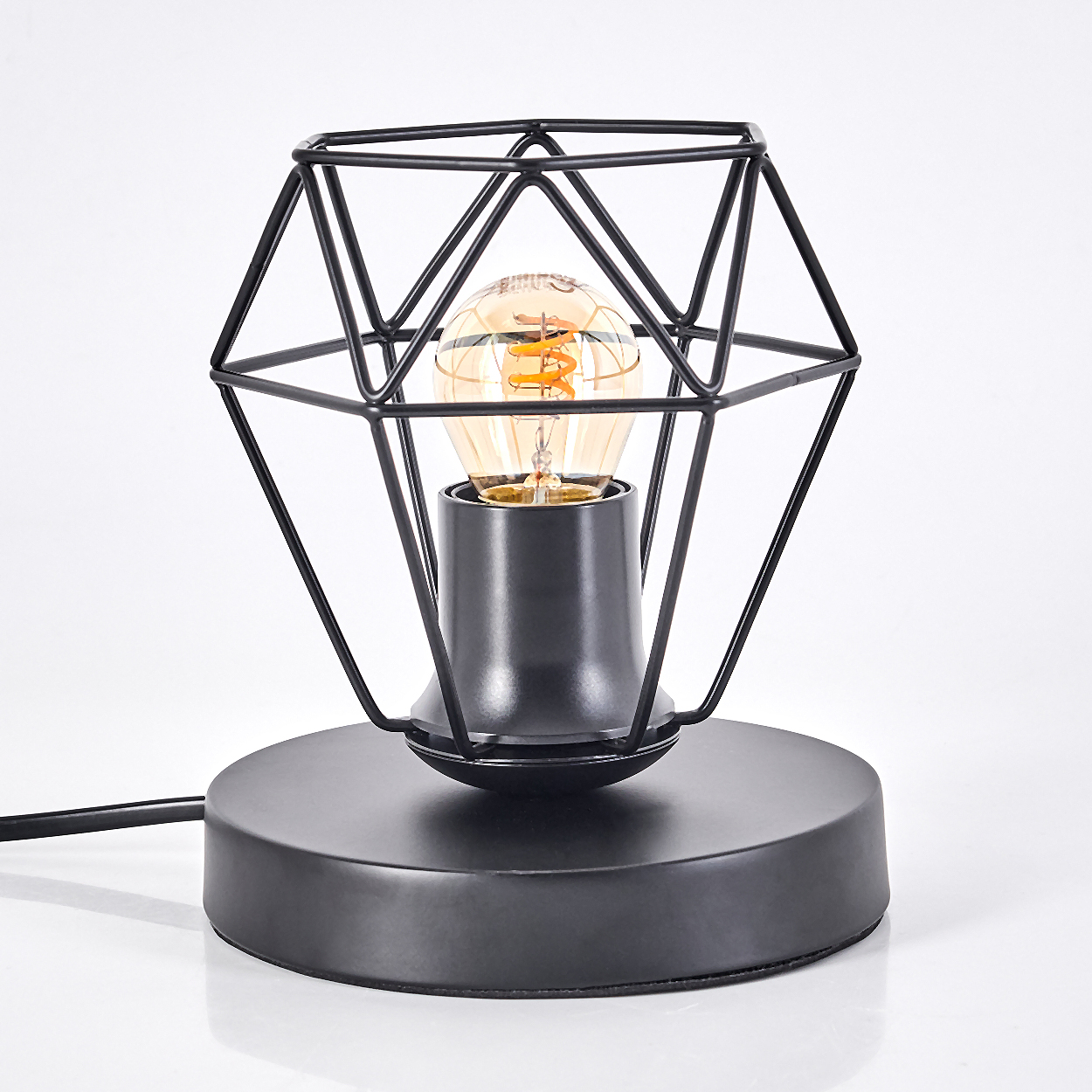 Eine schwarze Schreibtischlampe mit geometrischem Käfigdesign. Sie hat einen runden Sockel und eine Edison-Glühbirne. Der Hintergrund ist weiß.