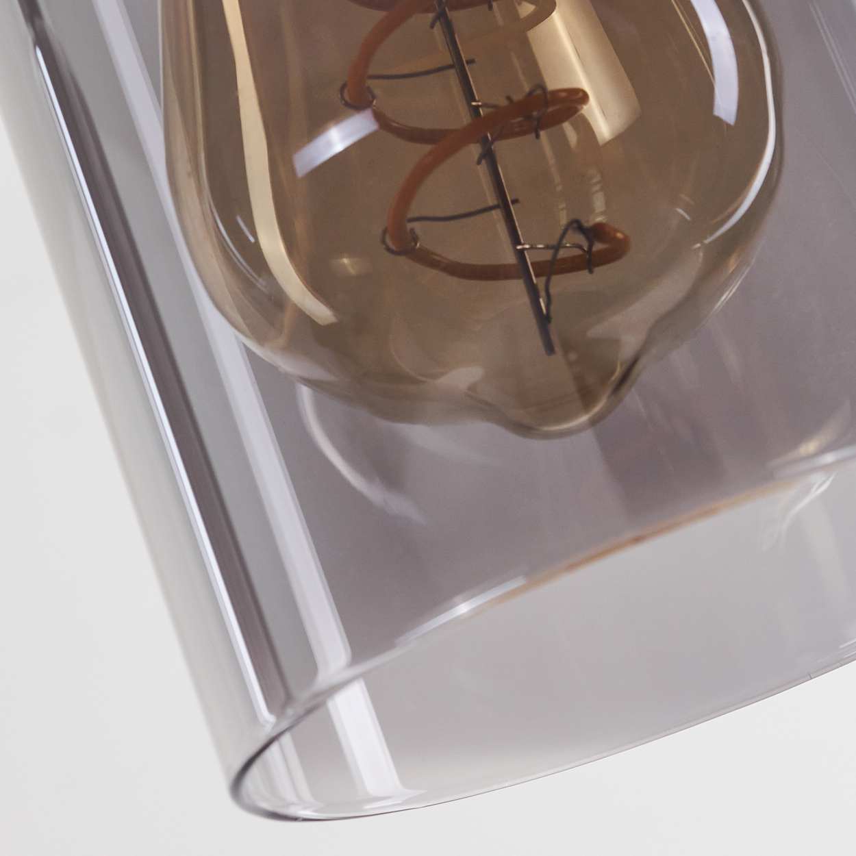 Nahaufnahme einer Leuchte. Eine große, braun getönte Glühbirne ist in einem transparenten, rechteckigen Schirm eingeschlossen. Der Hintergrund ist weiß.