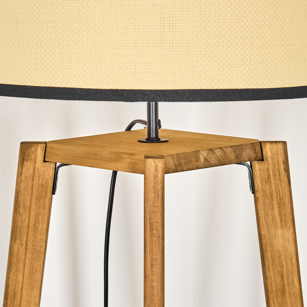 Holzlampensockel mit beigem Lampenschirm und schwarzem Rand. Die Lampe hat vier Holzbeine und ein schwarzes Kabel.