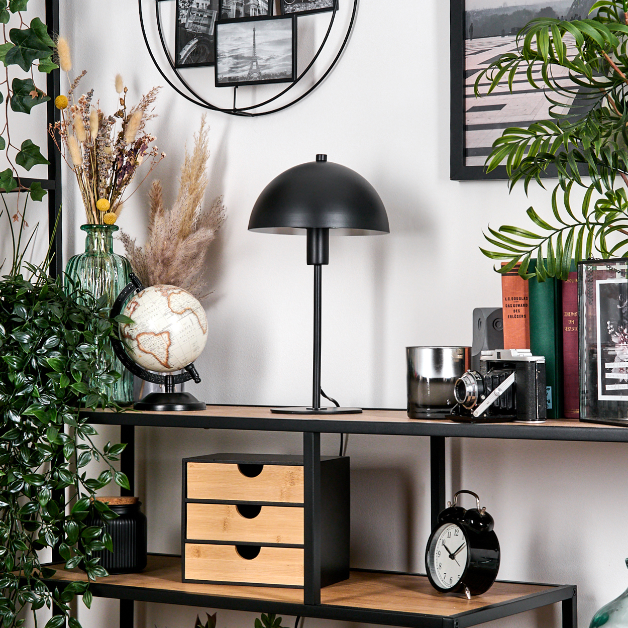 Ein Regal mit einer schwarzen Lampe, einem Globus, Büchern und einer Kamera. Es gibt auch eine Uhr und ein dreischubladiges Aufbewahrungssystem.