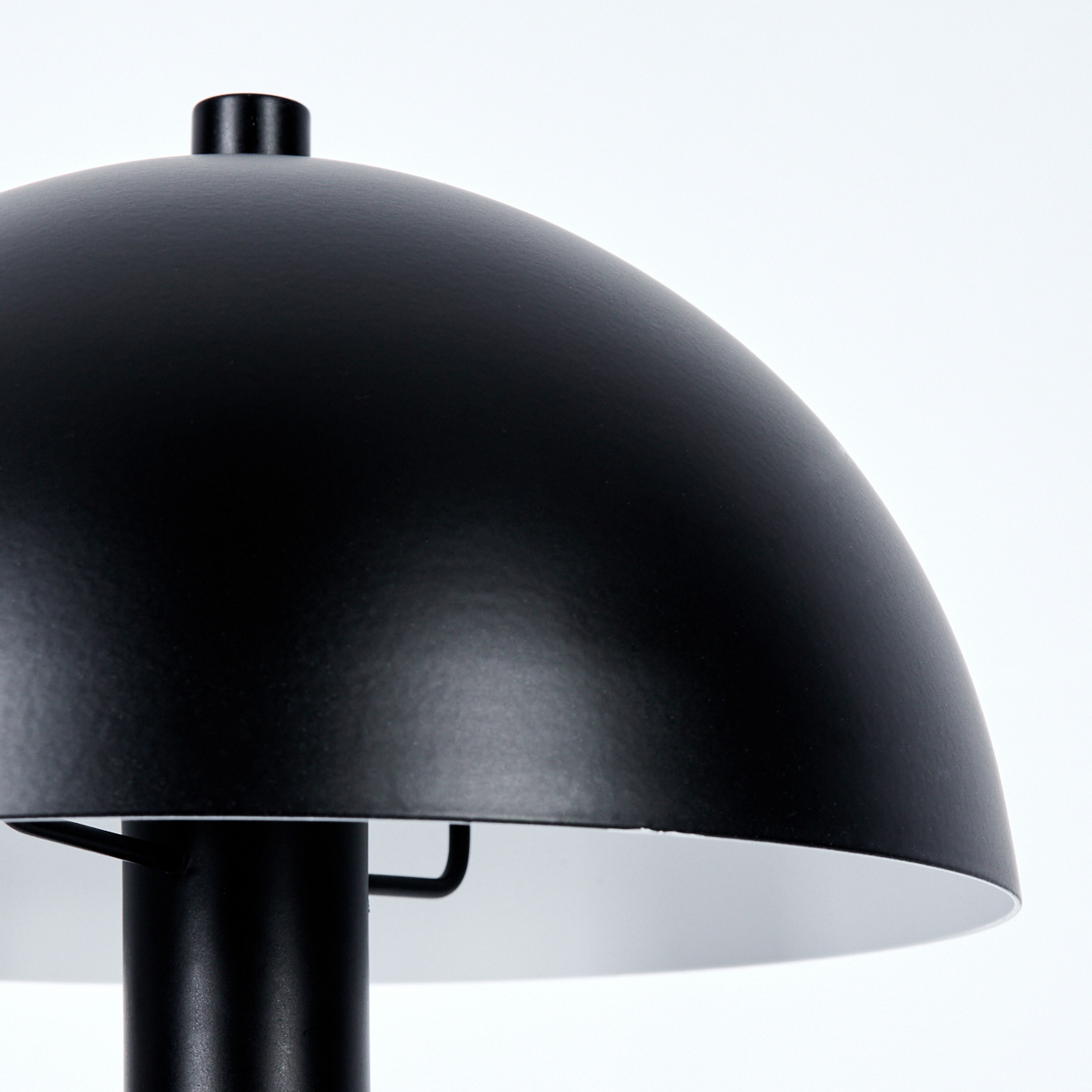 Eine schwarze Lampe mit einem kuppelförmigen Schirm. Die Innenseite ist weiß. Ein schwarzer Stiel stützt den Schirm. Der Hintergrund ist weiß.