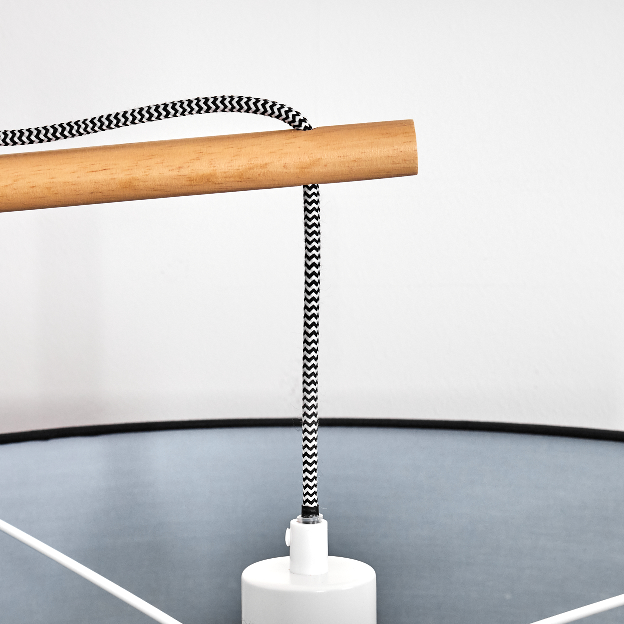 Ein Holzstab mit einem schwarz-weißen Zickzack-Kabel. Darunter eine weiße Lampe und im Hintergrund ein hellblauer Lampenschirm.