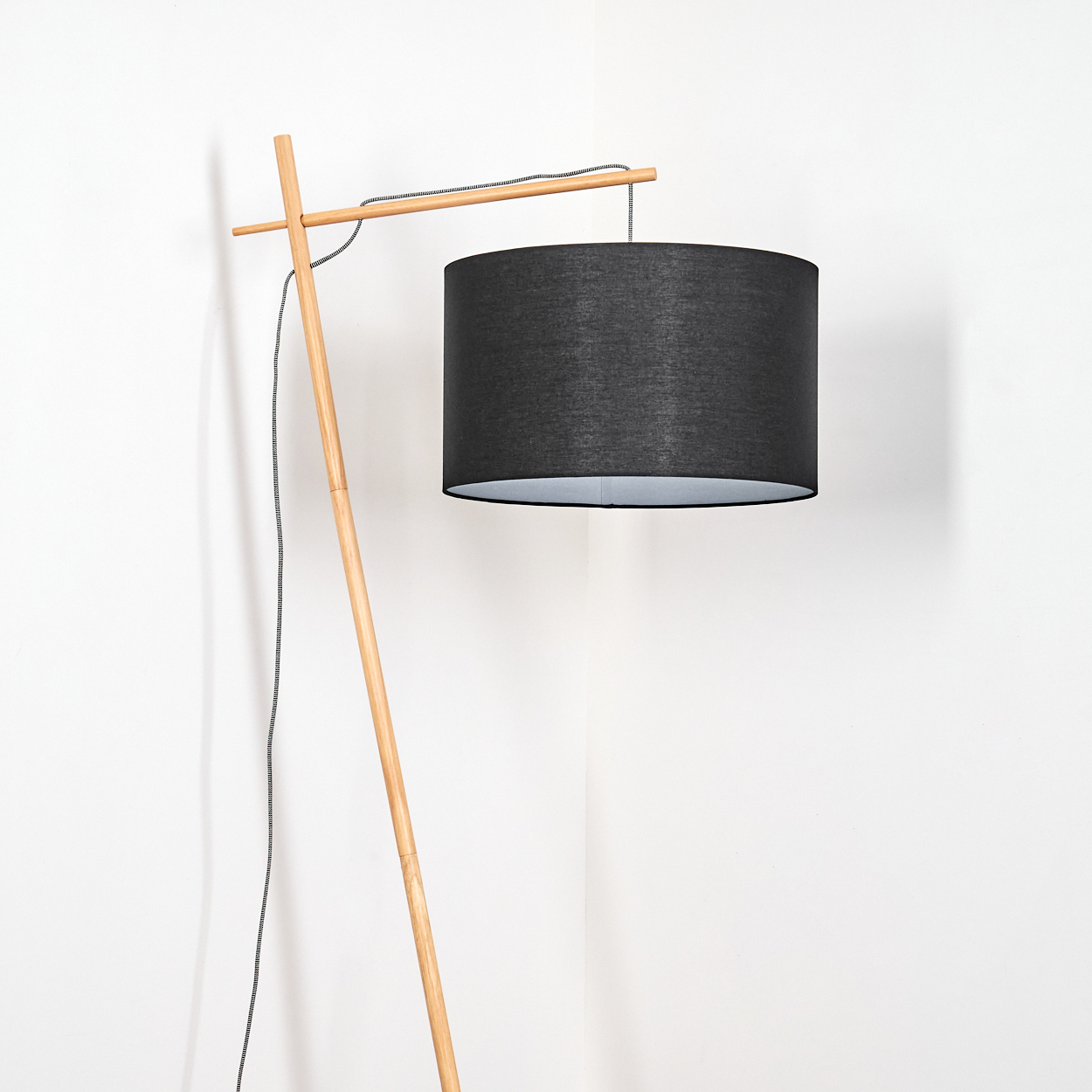 Eine moderne Stehlampe mit schwarzem Lampenschirm und Holzrahmen steht vor einer weißen Wand.
