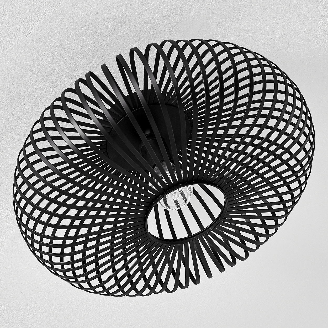 Eine schwarze, spiralförmige Deckenlampe mit sichtbarer Glühbirne hängt von einer weißen Decke. Die Lampe hat ein offenes Design.