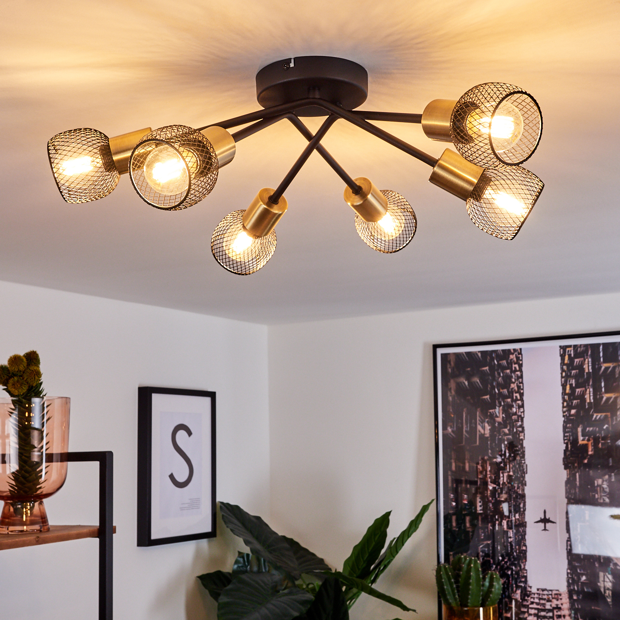 Deckenleuchte mit acht Lampen. Gold- und Schwarz-Armatur. Innenraum mit Kunst und Pflanzen.
