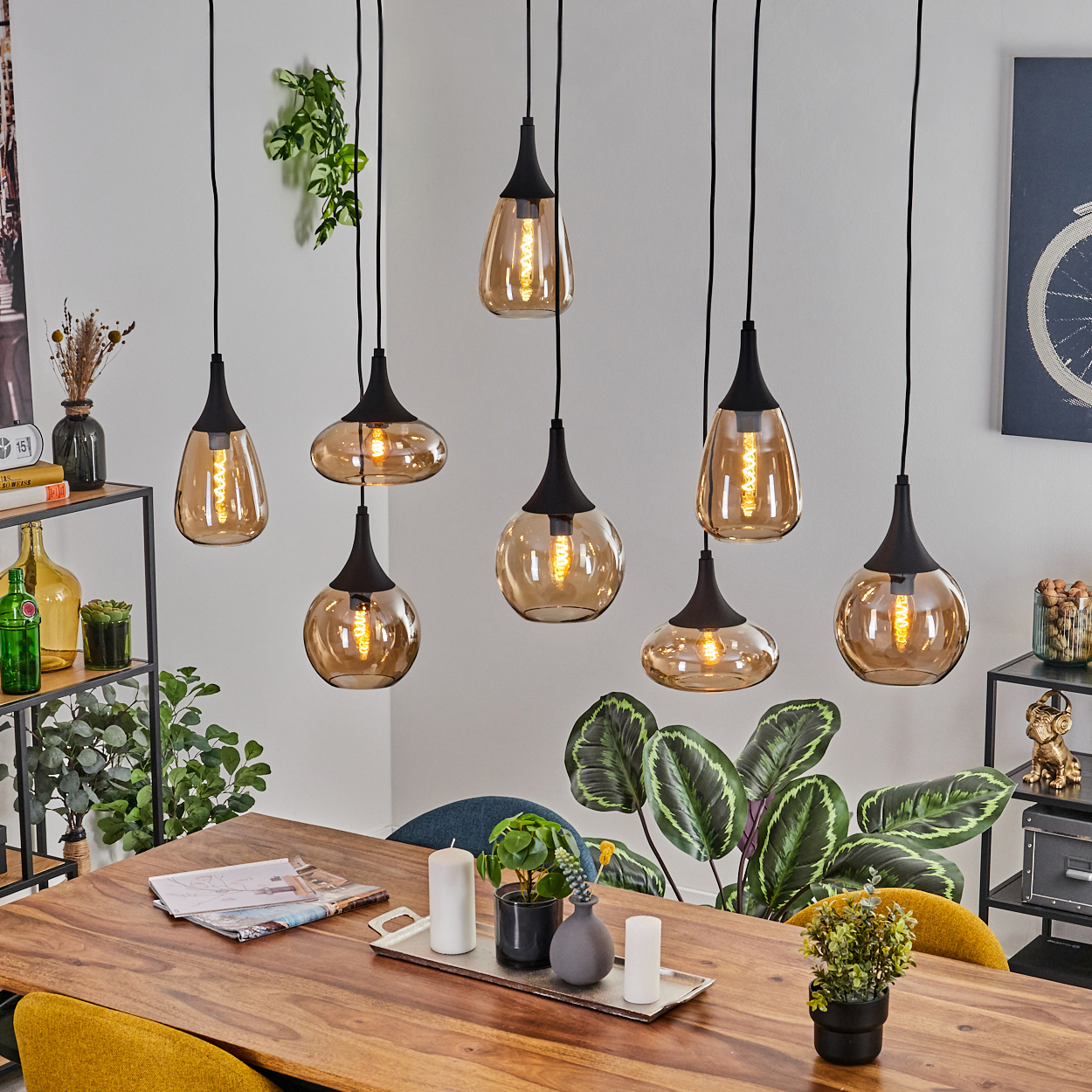 Ein Esszimmer mit Holztisch, Pendelleuchten und Pflanzen. Die Leuchten sind bernsteinfarben mit schwarzen Armaturen. Pflanzen schmücken den Raum.