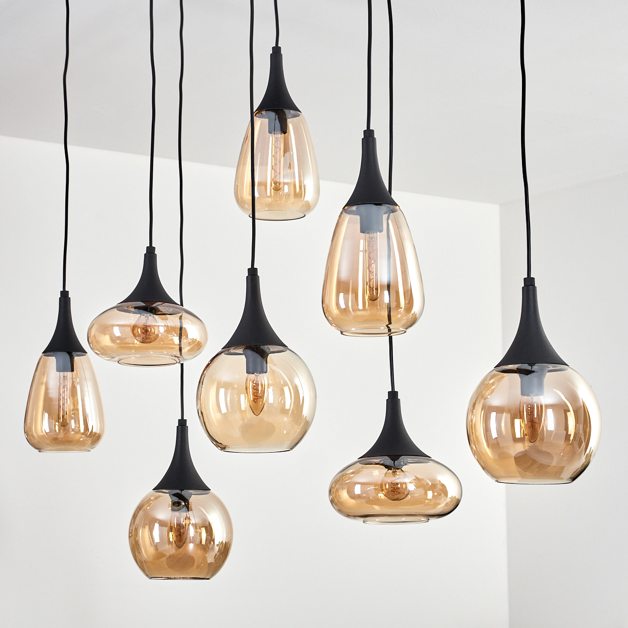 Neun Pendelleuchten mit bernsteinfarbenen Glasschirmen und schwarzen Halterungen hängen von einer weißen Decke. Jede hat eine Glühbirne.
