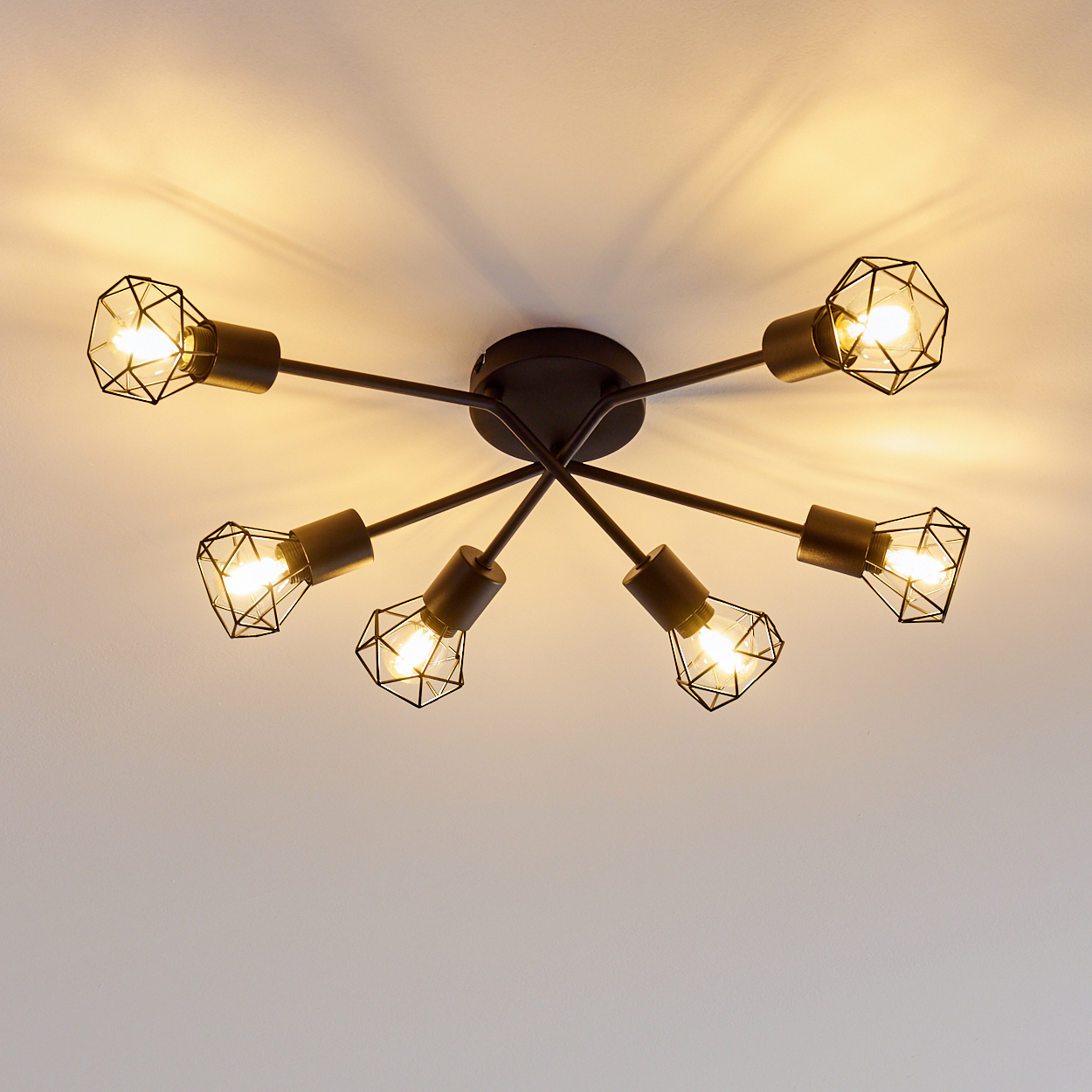 Eine moderne Deckenleuchte mit sechs Glühbirnen. Jede Glühbirne ist in einem geometrischen Käfig eingeschlossen und strahlt warmes Licht aus.