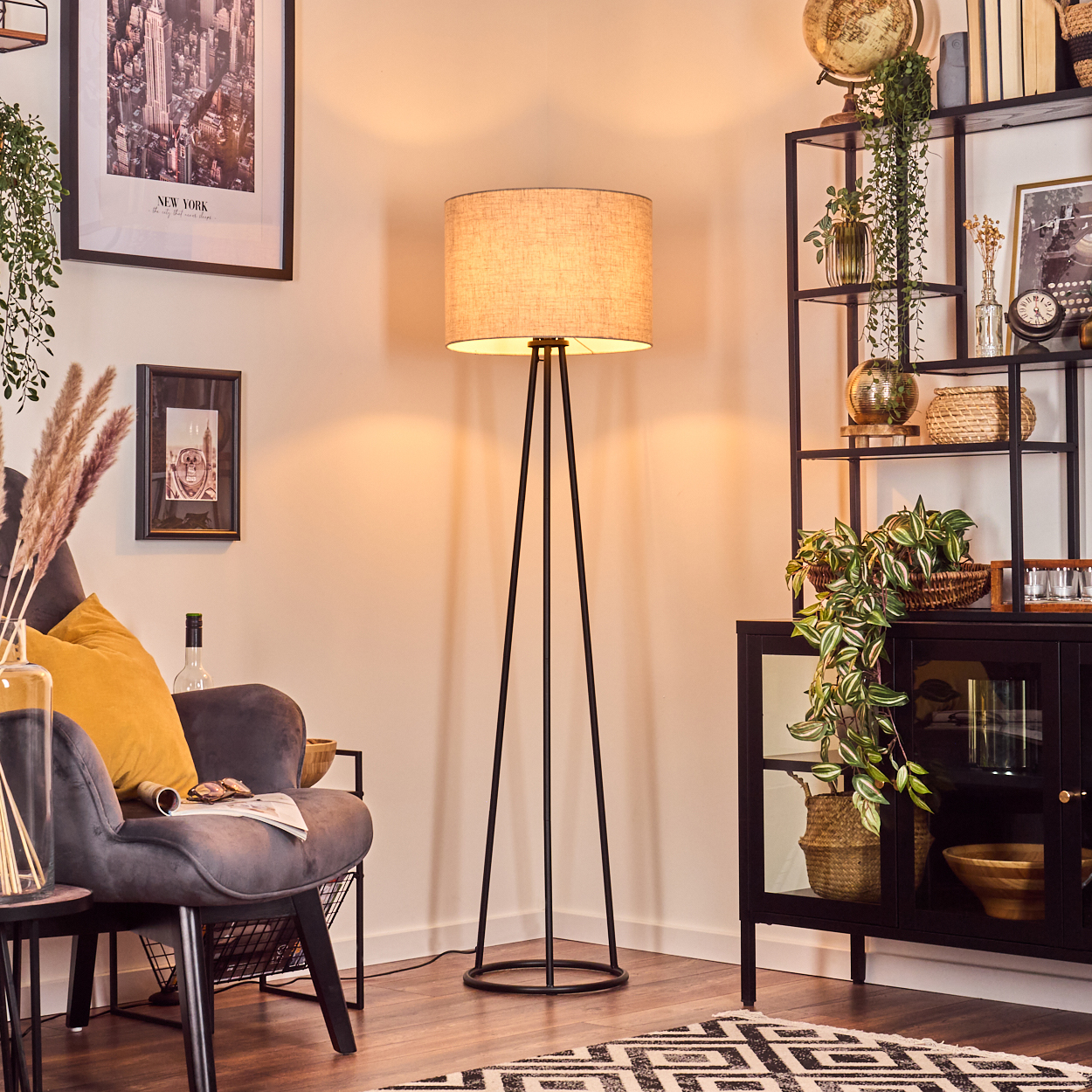 Ein Wohnzimmer mit Stehlampe, Sessel und Regal. Die Einrichtung umfasst Pflanzen, Bilder und einen Teppich. Ein gemütlicher und einladender Raum.