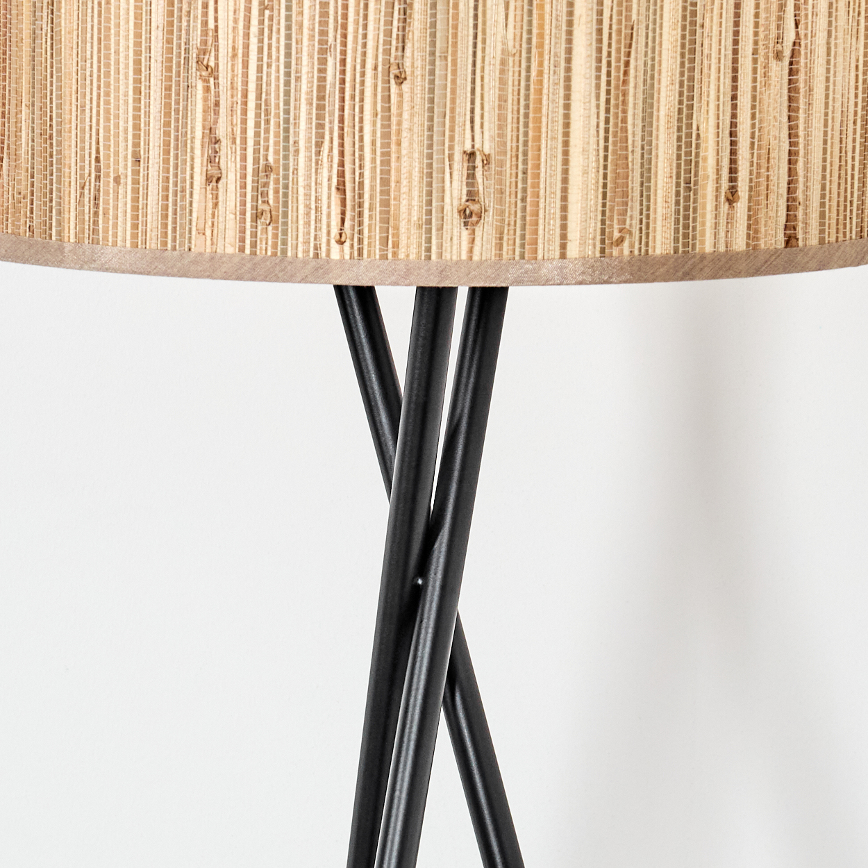 Nahaufnahme einer Lampe. Der Lampenschirm ist aus gewebtem, hellbraunem Material. Schwarze Beine stützen den Lampenschirm vor einem weißen Hintergrund.