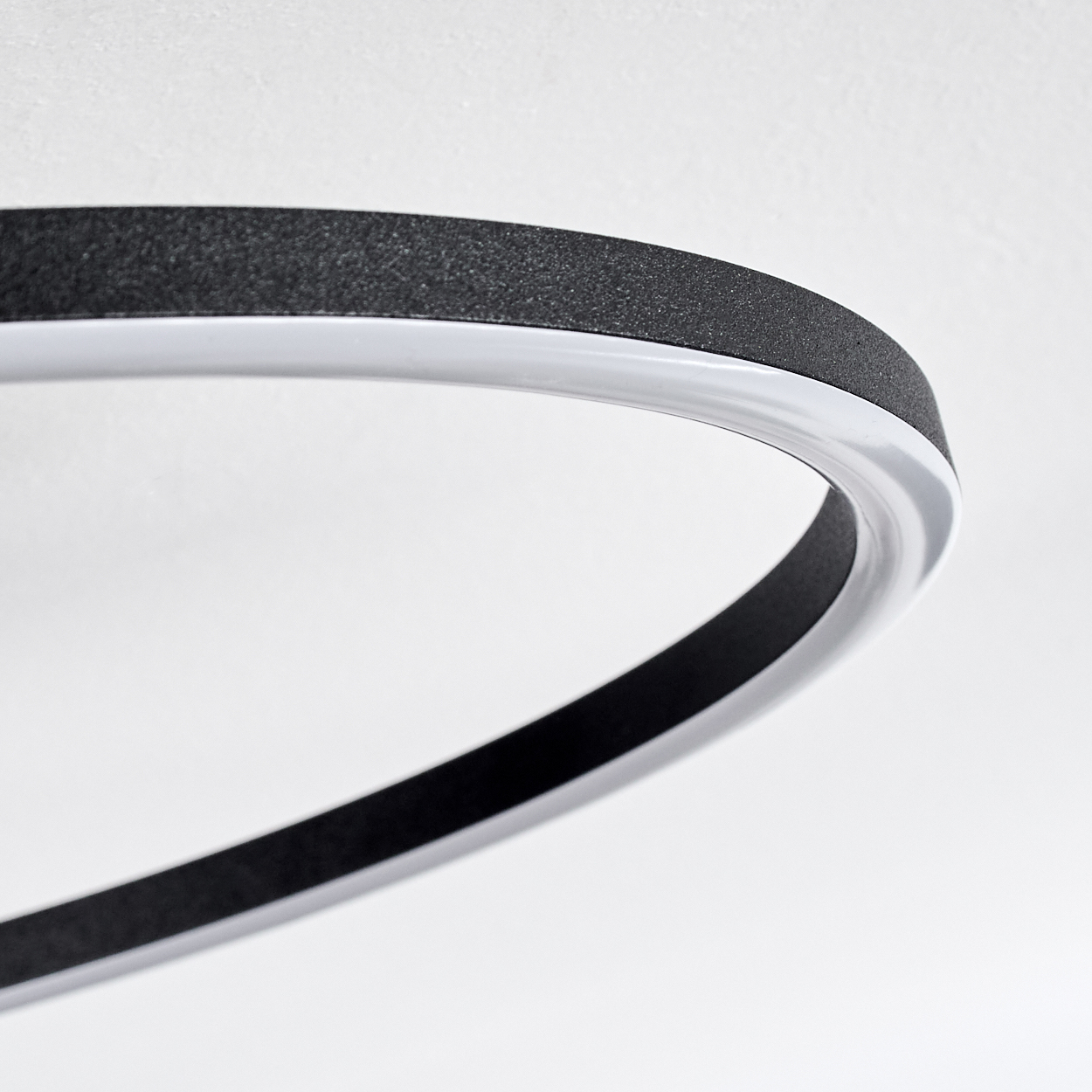 Nahaufnahme einer modernen, oval geformten Leuchte. Die Leuchte hat eine schwarze, strukturierte Oberseite und eine weiße, gebogene Basis auf weißem Hintergrund.