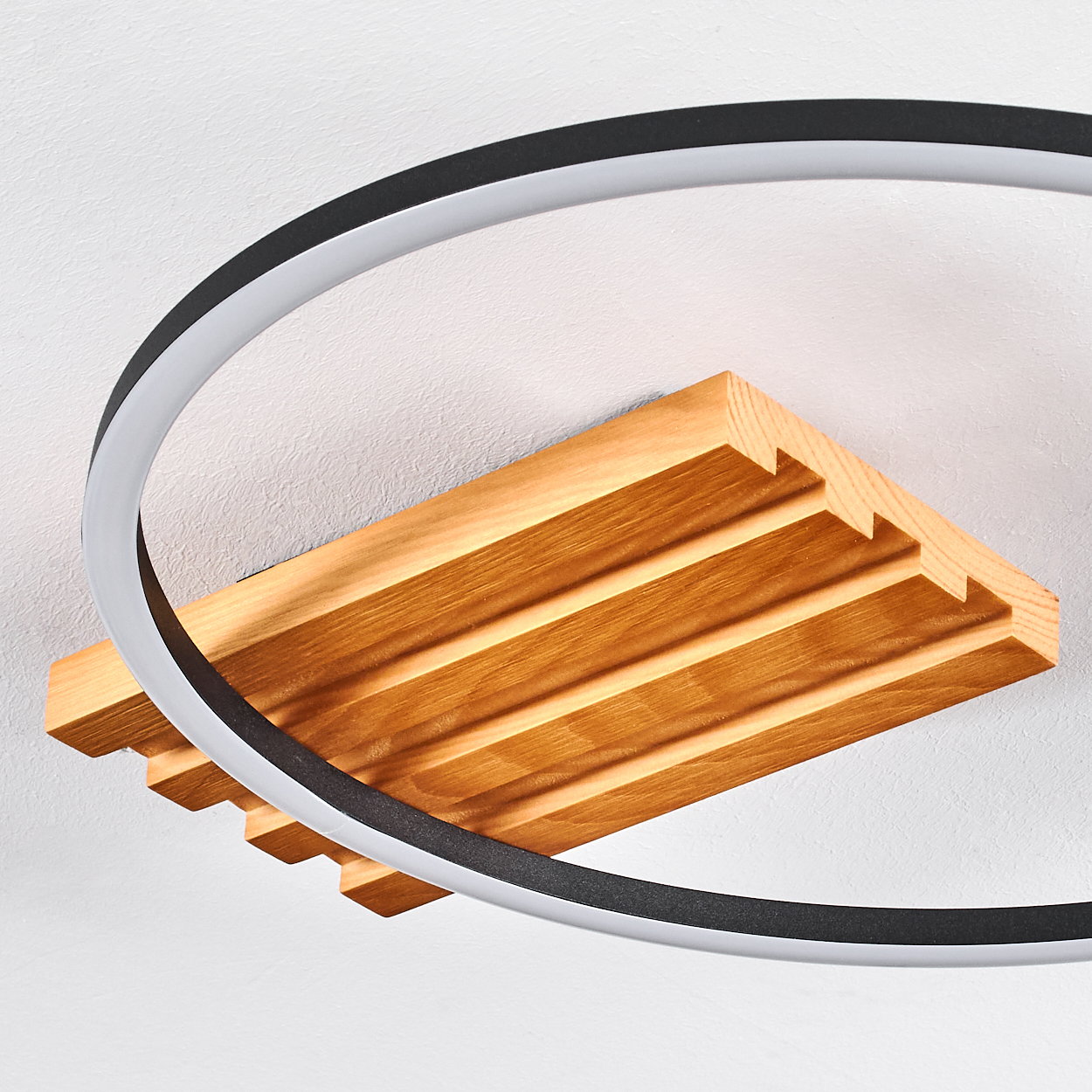 Eine Holzleuchte. Eine Holzkiste mit parallelen Rillen ist an der Decke befestigt. Darüber befindet sich ein gebogenes Licht.