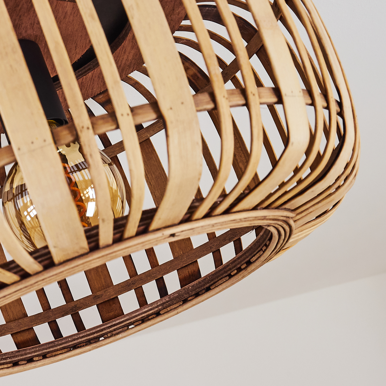 Nahaufnahme eines geflochtenen Lampenschirms aus Rattan mit sichtbarer Glühbirne. Der Hintergrund ist eine weiße Decke.