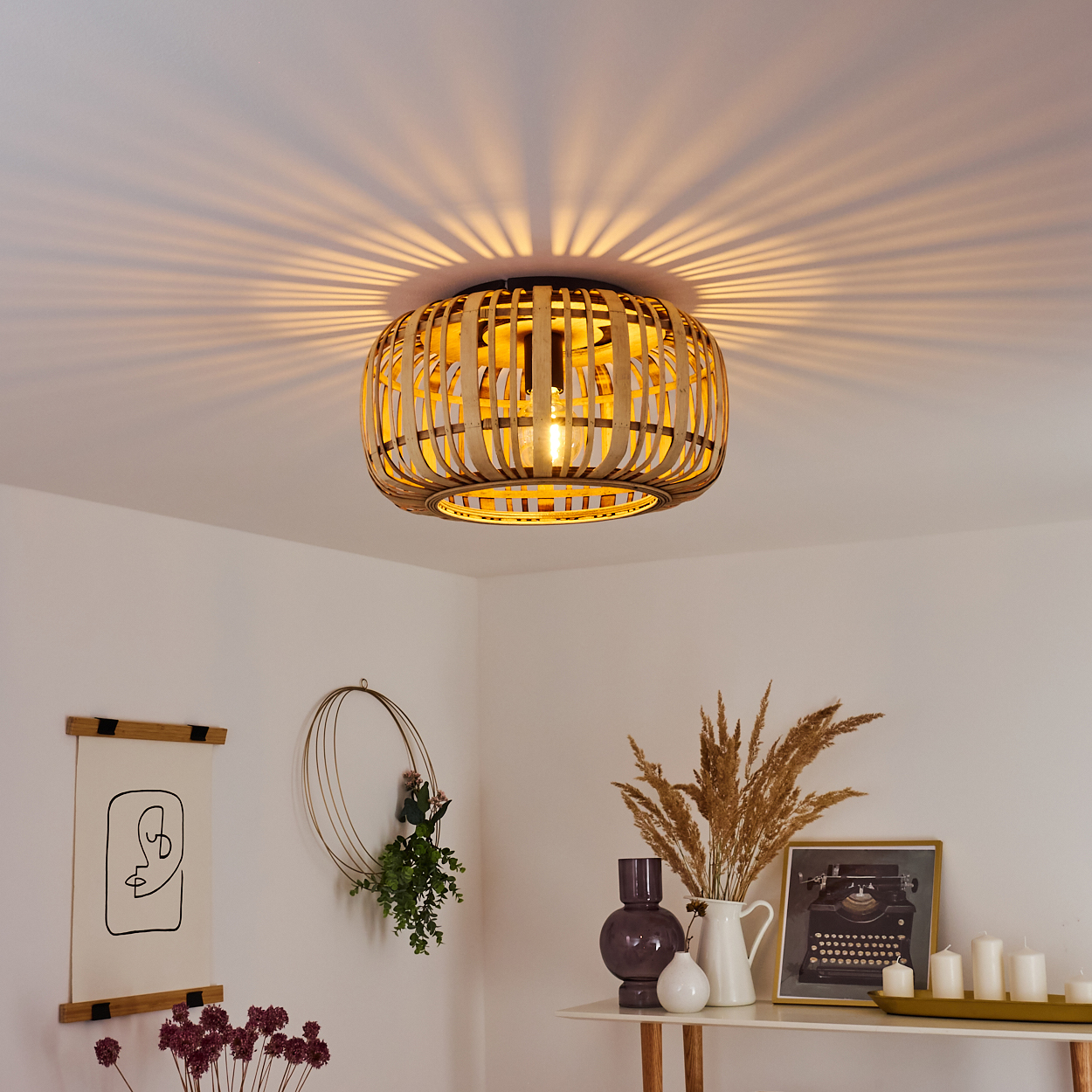 Ein Bambus-Lampenschirm hängt an der Decke und wirft ein Lichtmuster. Darunter befindet sich ein Regal mit Dekorationen wie einer Schreibmaschinen-Bild und Vasen.