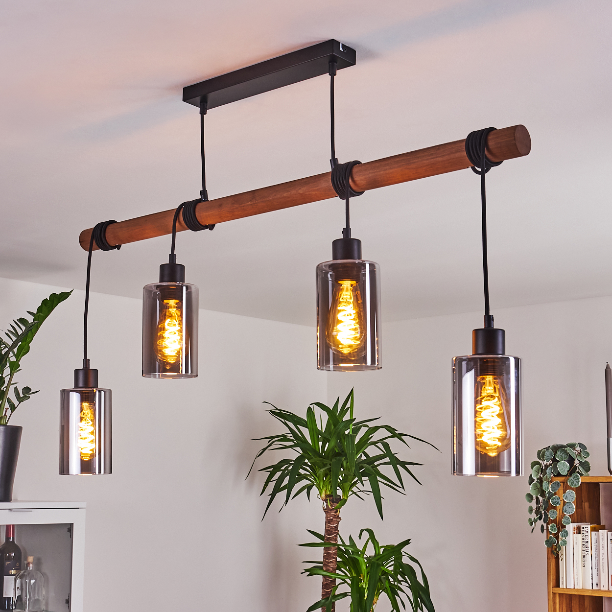 Eine moderne Pendelleuchte mit vier Lampen. Die Leuchte umfasst einen Holzbalken und transparente Glasschirme mit sichtbaren Glühbirnen.
