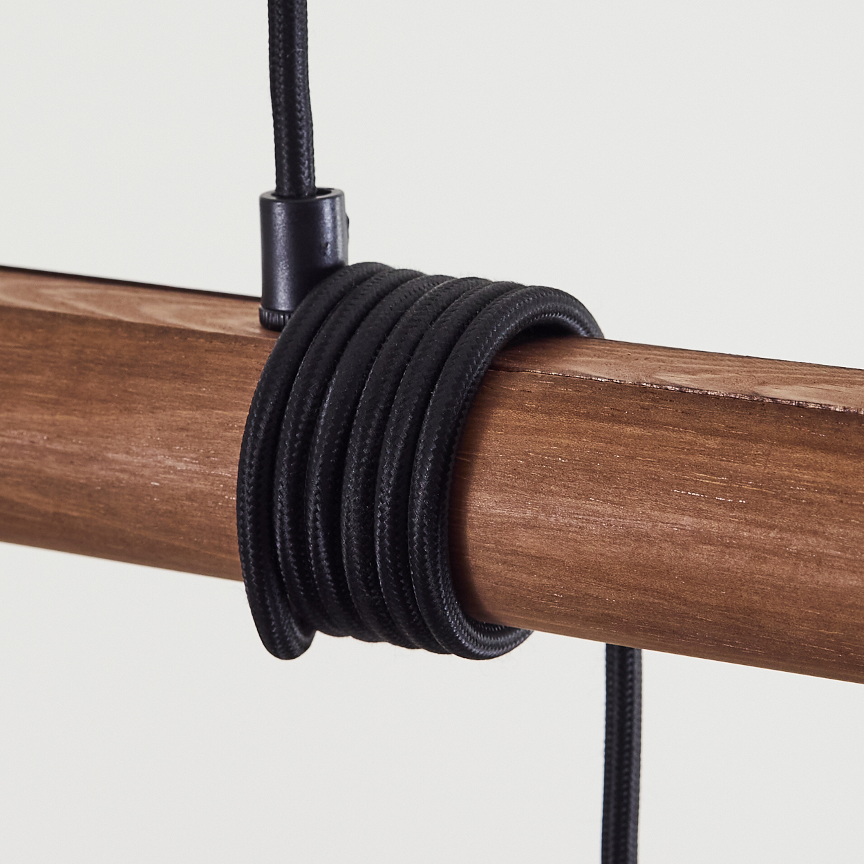 Nahaufnahme eines Holzbalkens, um den ein schwarzes Kabel gewickelt ist. Das Kabel ist dick und strukturiert. Der Hintergrund ist weiß.